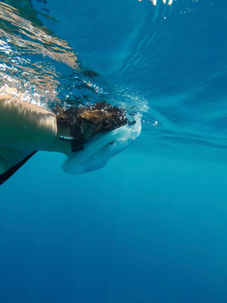 A woman snorkeling underwater with a full-face mask