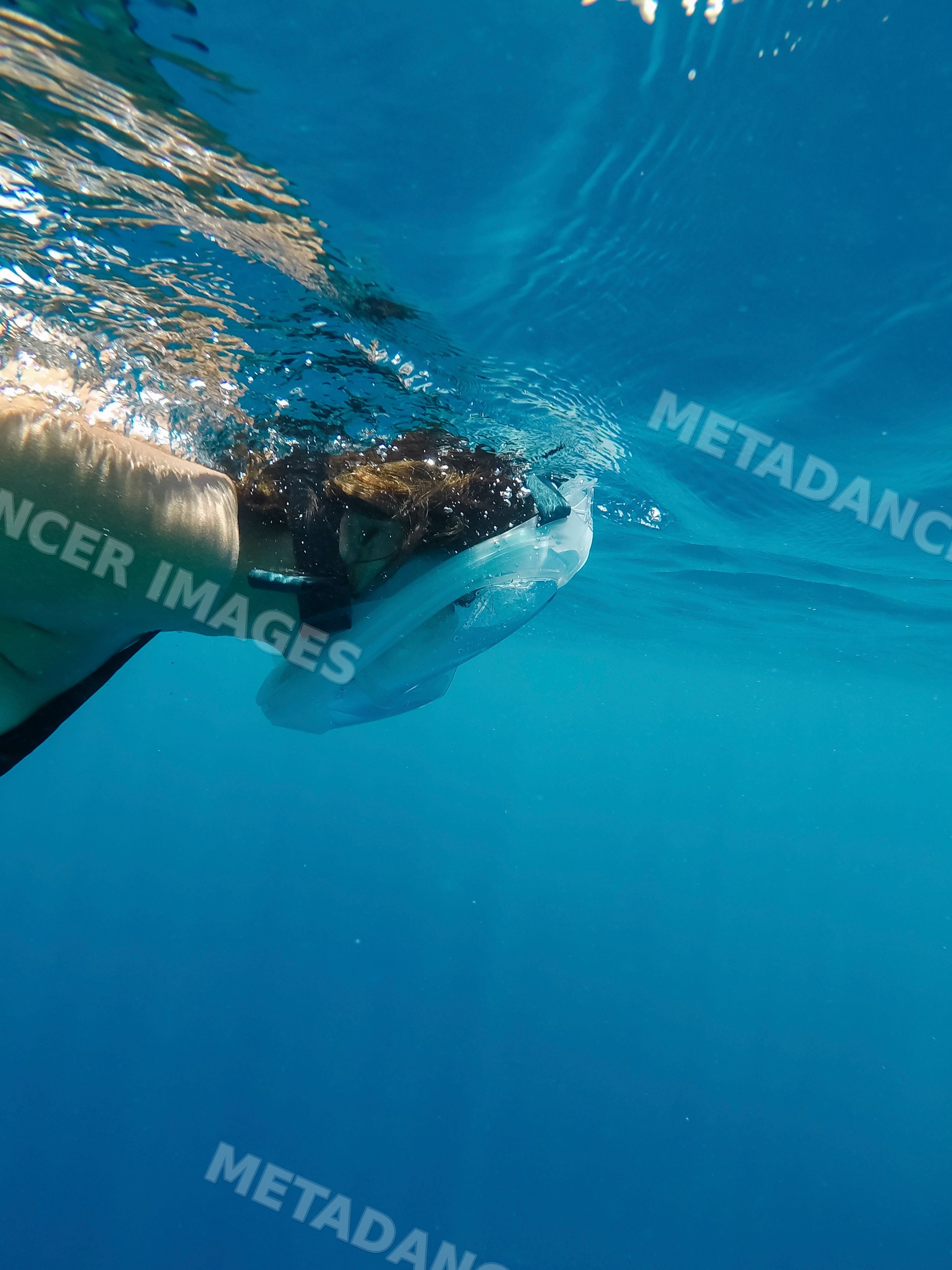 A woman snorkeling underwater with a full-face mask