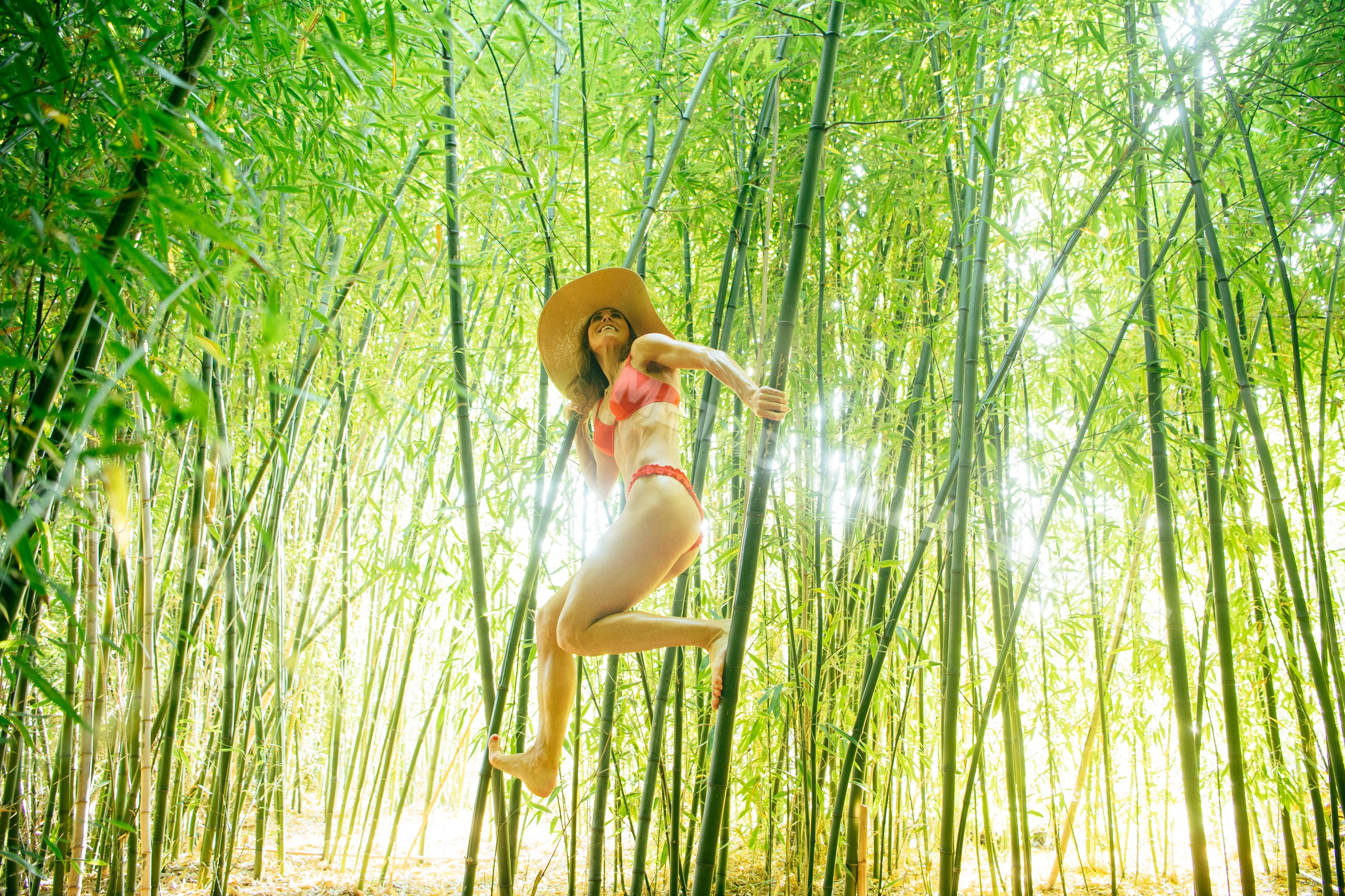 White woman climbing bamboo stalks in green bamboo forest outdoors