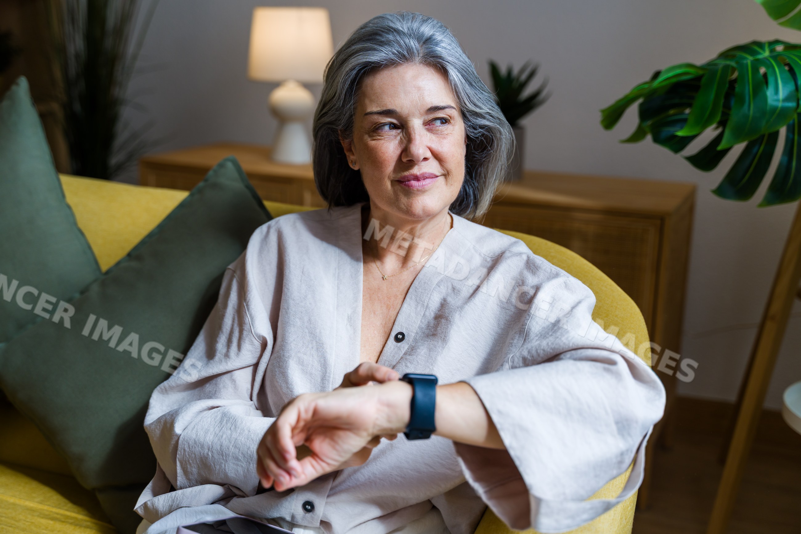Mature white woman sitting on yellow sofa looking contemplatively