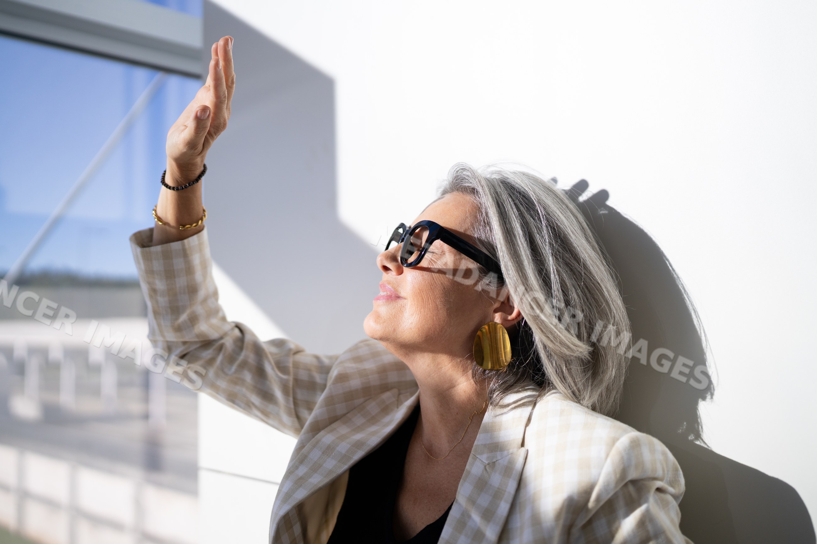 White woman with sunglasses and checkered blazer enjoying sunlight