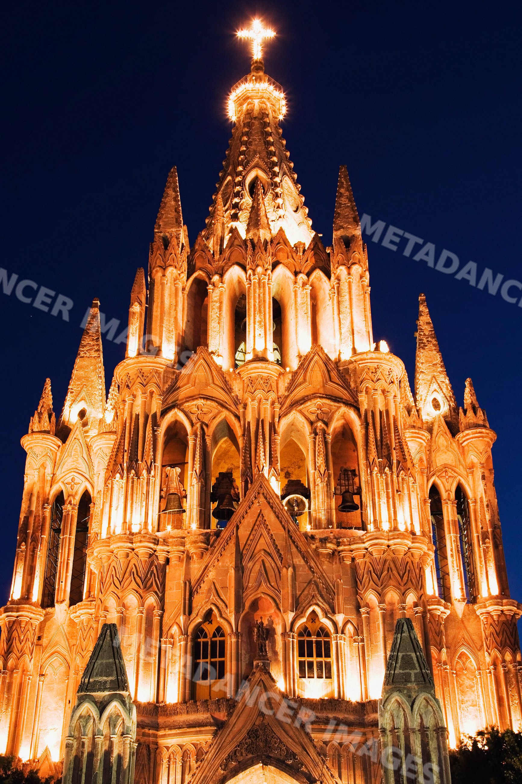 Illuminated church facade with stone spires and cross at night