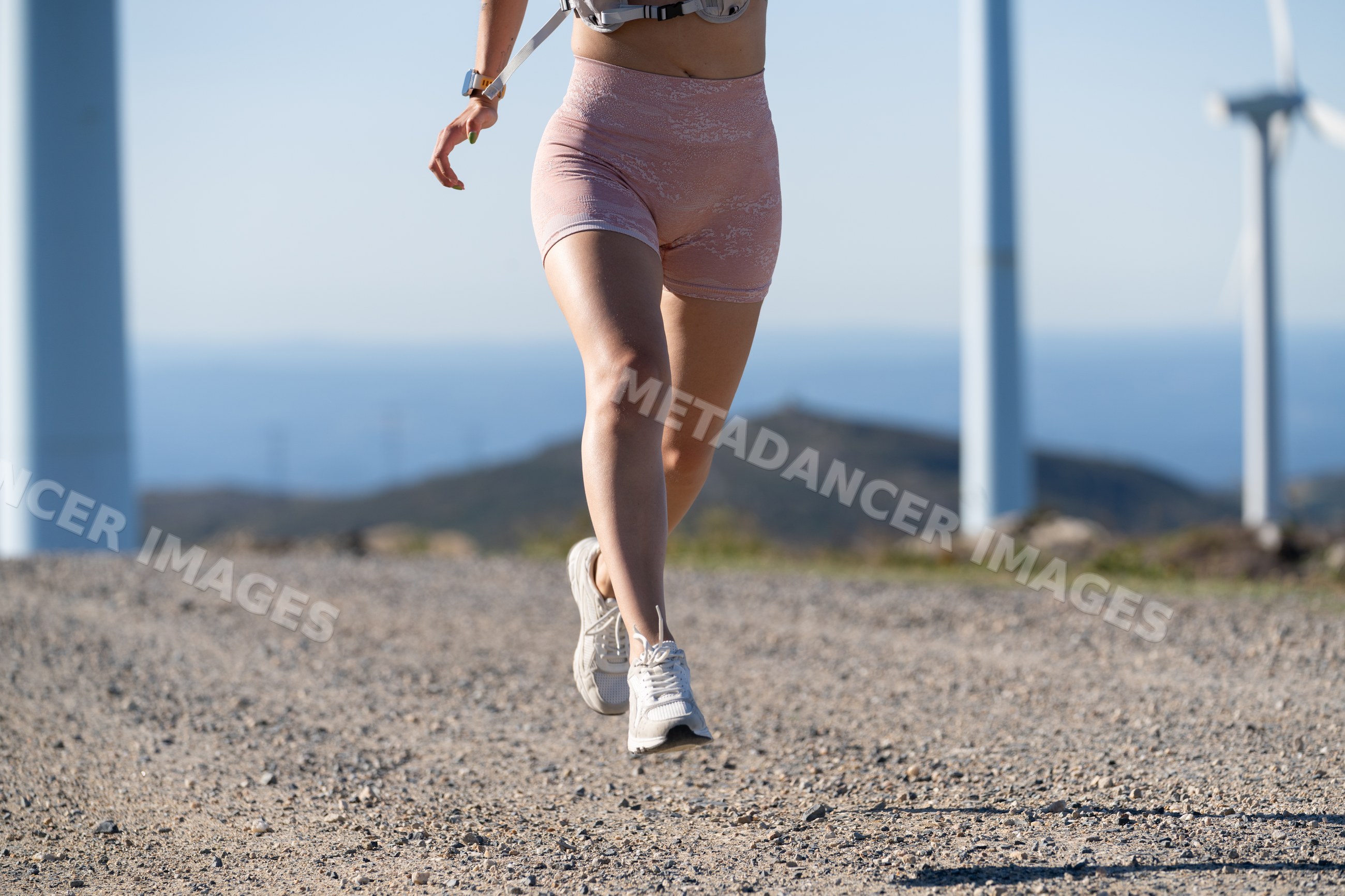 White Woman running on a gravel trail near wind turbines in Galicia