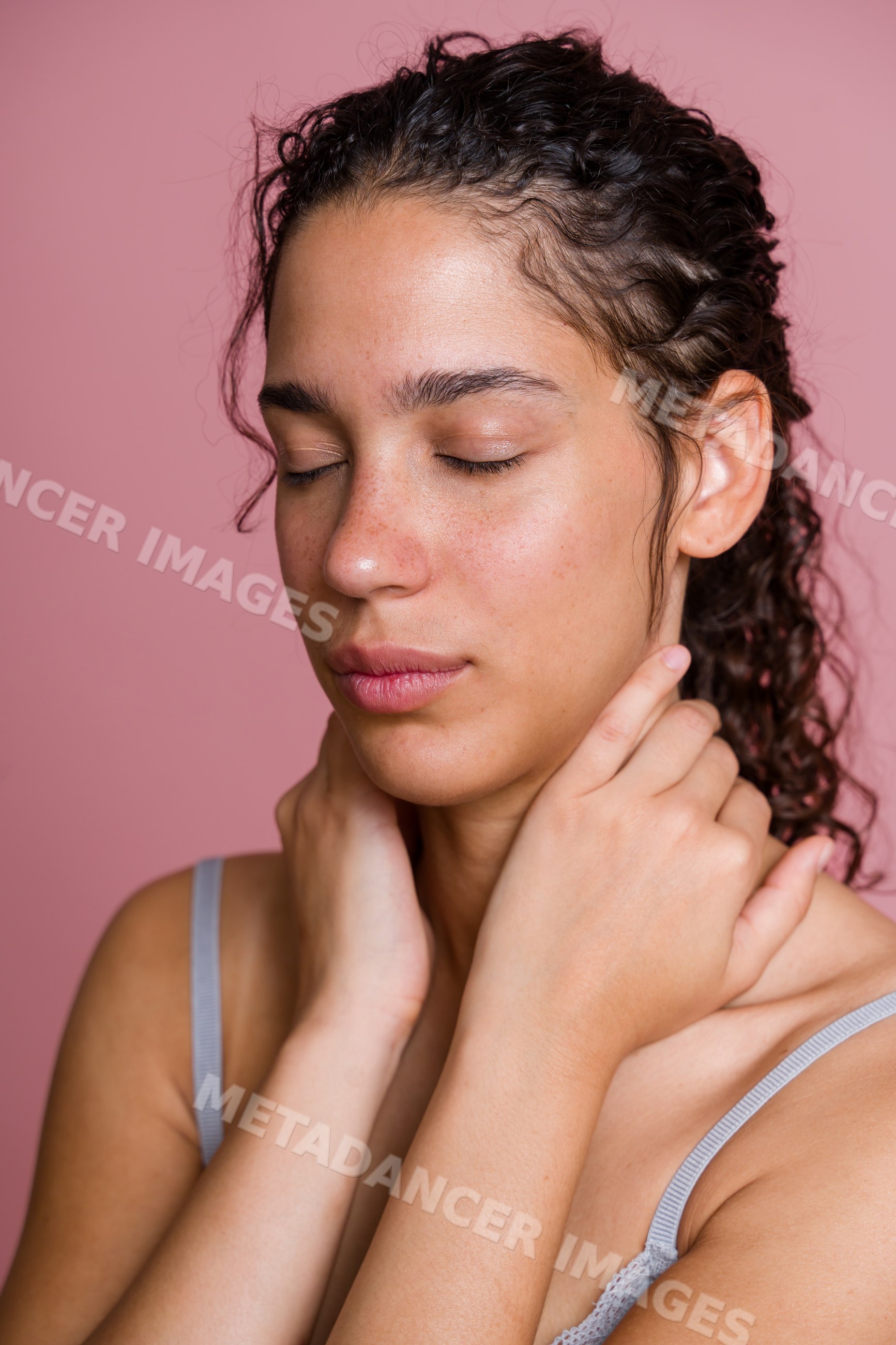 Hispanic woman with closed eyes and curly hair touching her neck