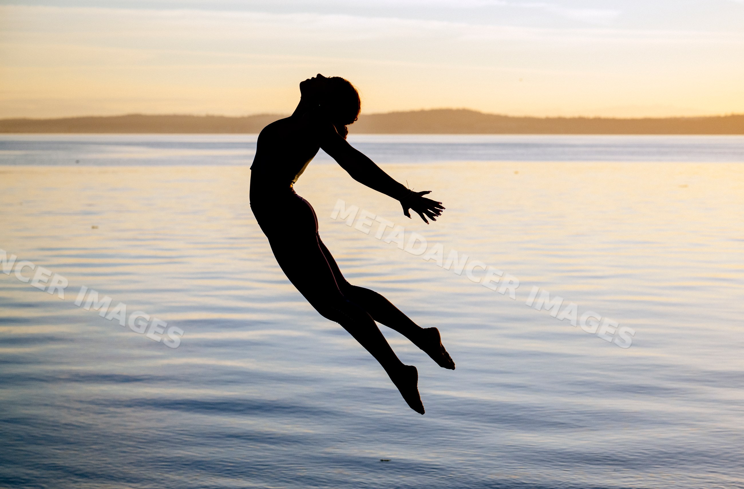 Hispanic woman jumping in yoga pose by lake at sunset