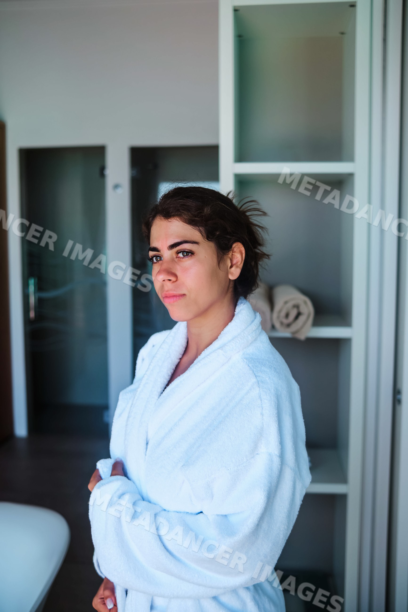 A woman wearing a white bathrobe stands indoors in a bathroom