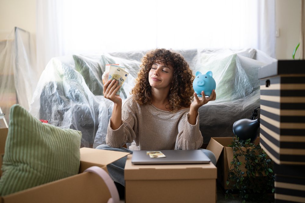 White woman saving money with piggy bank during moving in living room