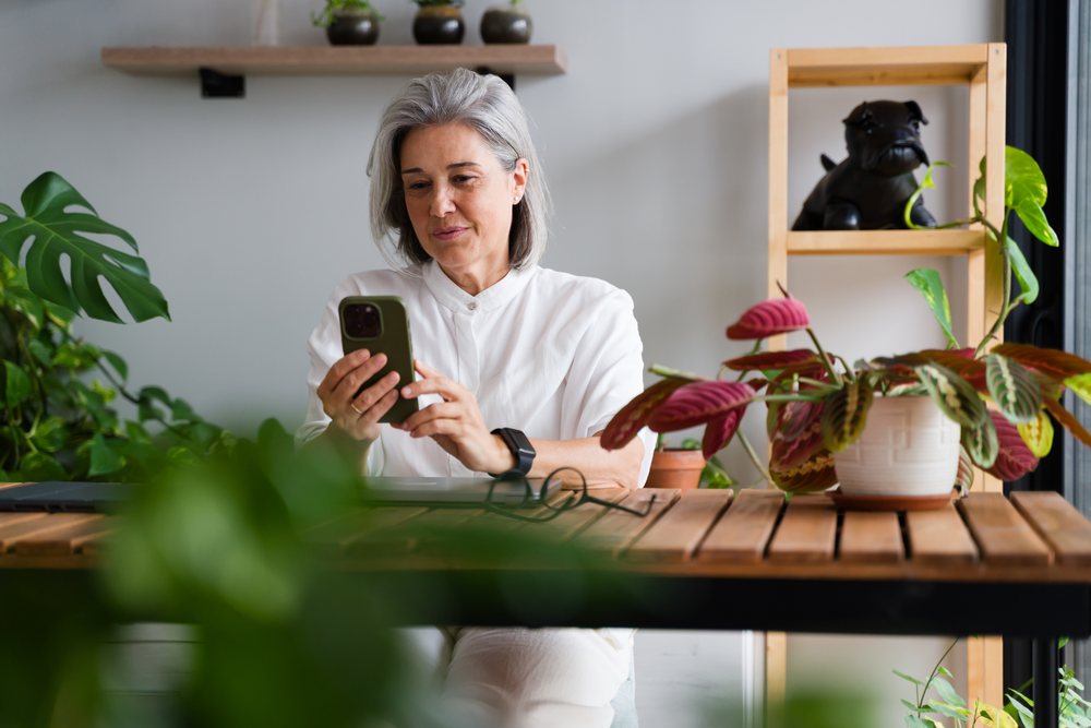 White Woman using smartphone indoors with houseplants and wooden table