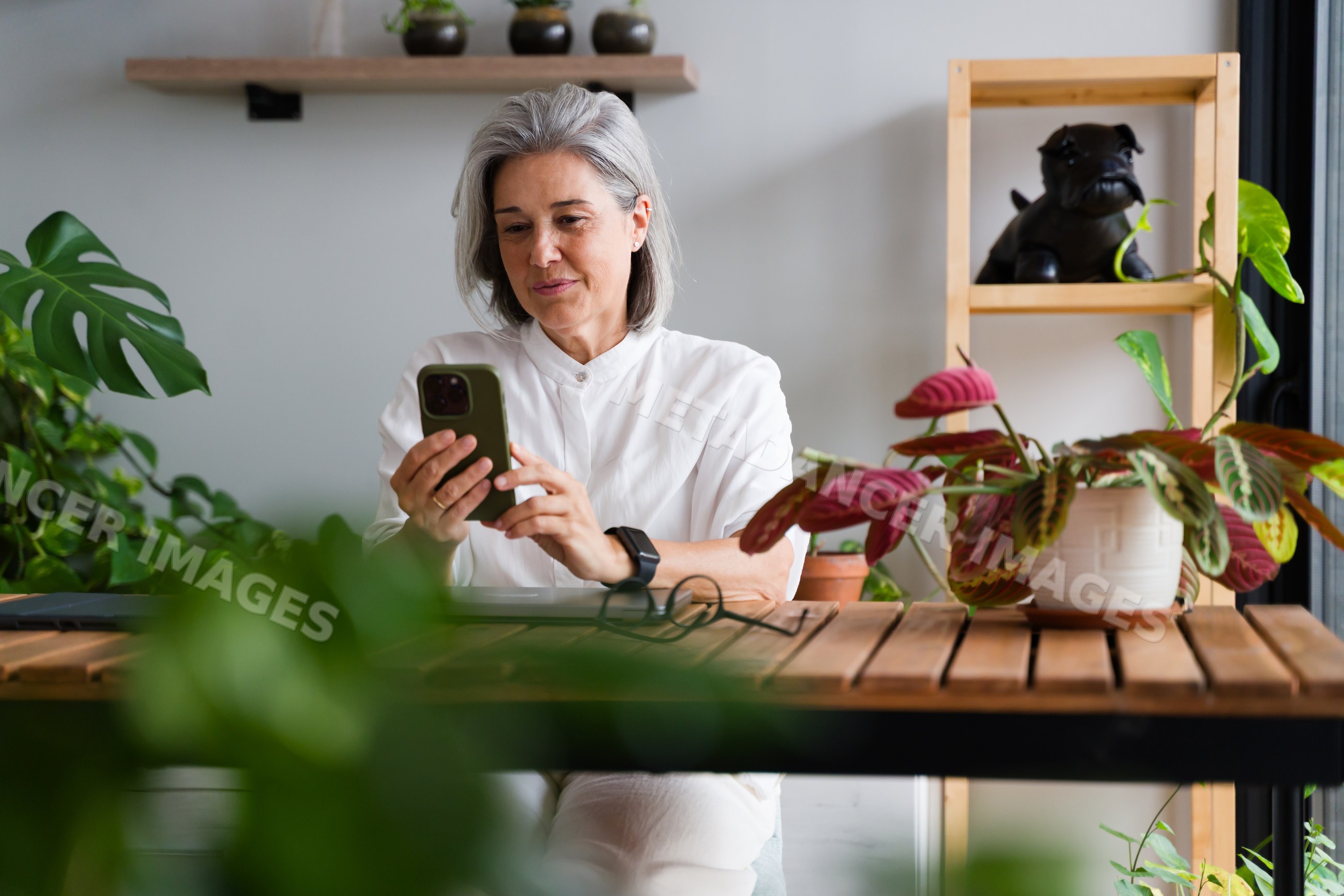 White Woman using smartphone indoors with houseplants and wooden table