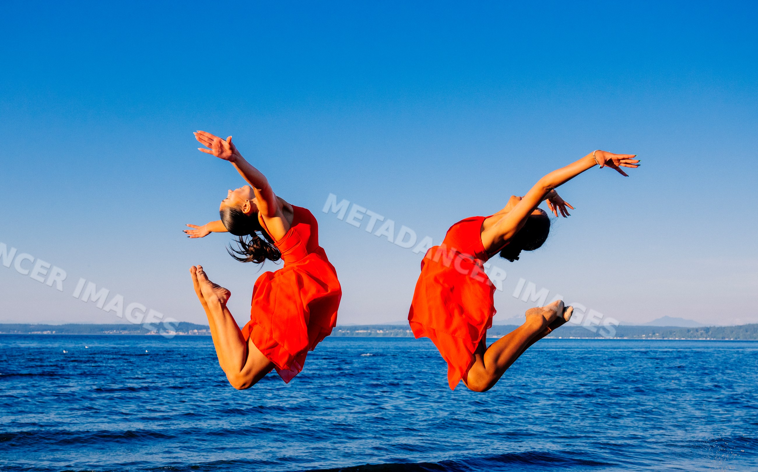 Two women in red dresses jump in acrobatic poses by the ocean shore