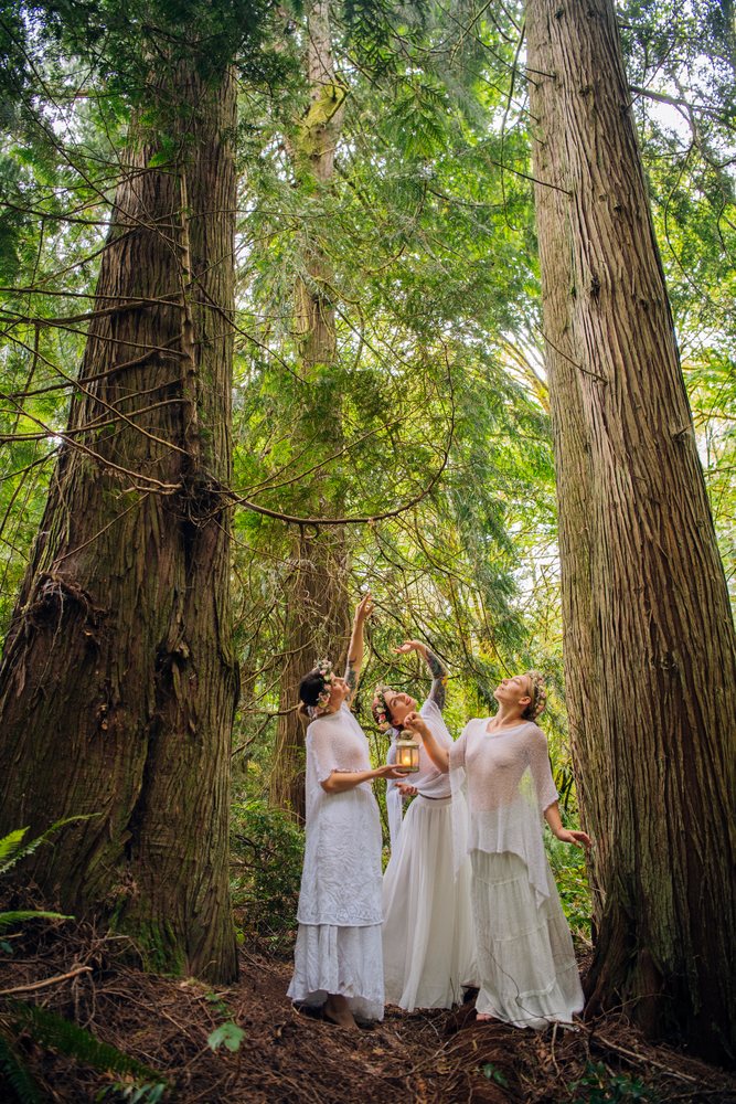 Three white women with lantern and floral crowns in forest