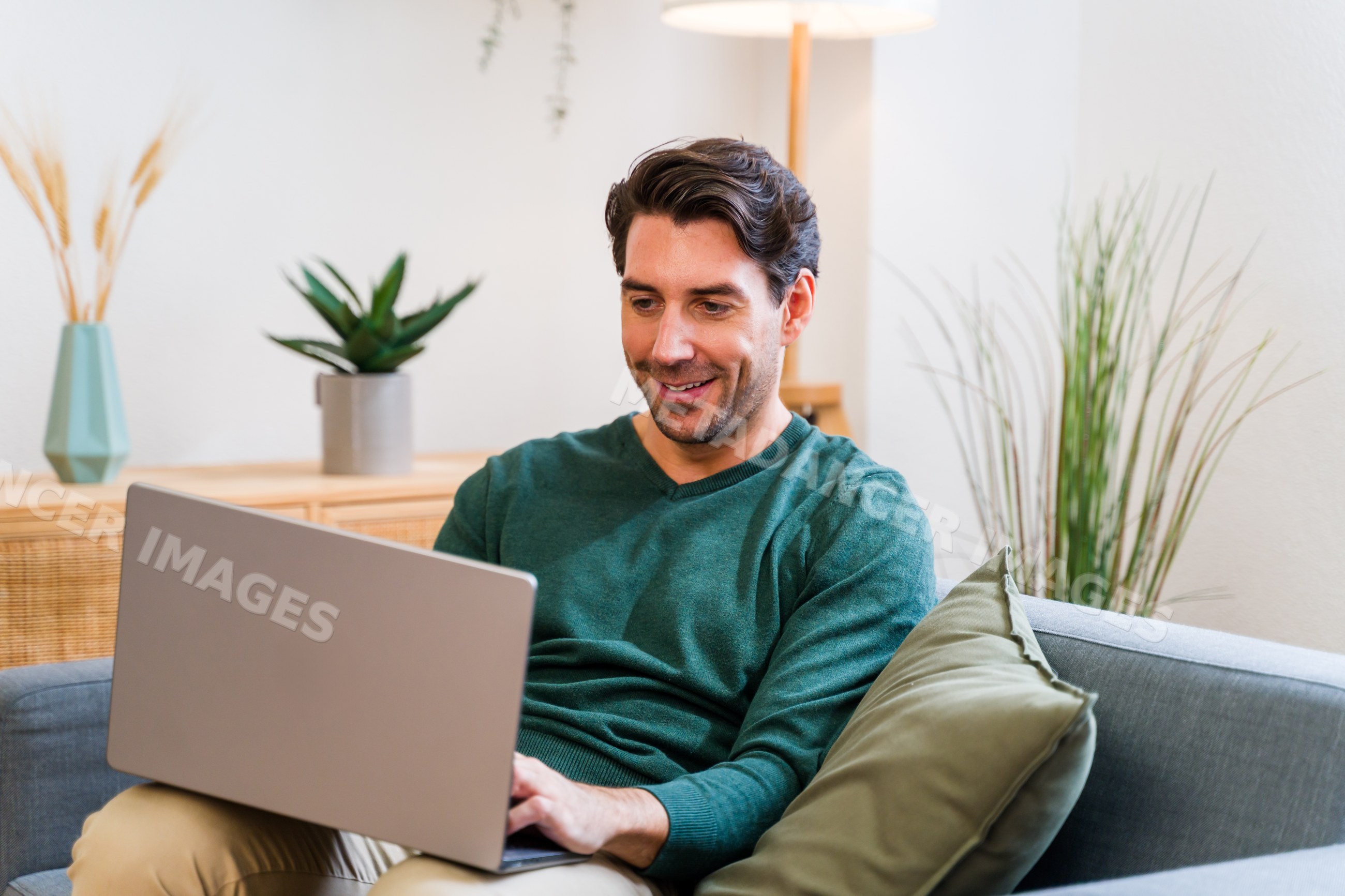 White man sitting on gray couch using laptop in modern living room