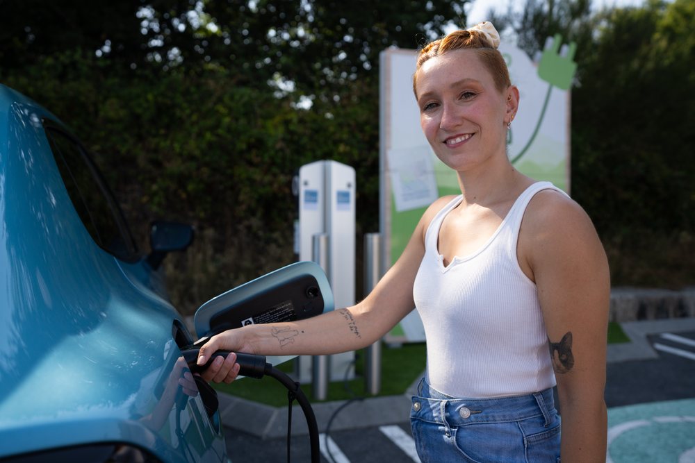 A white woman charges her electric car at an outdoor station