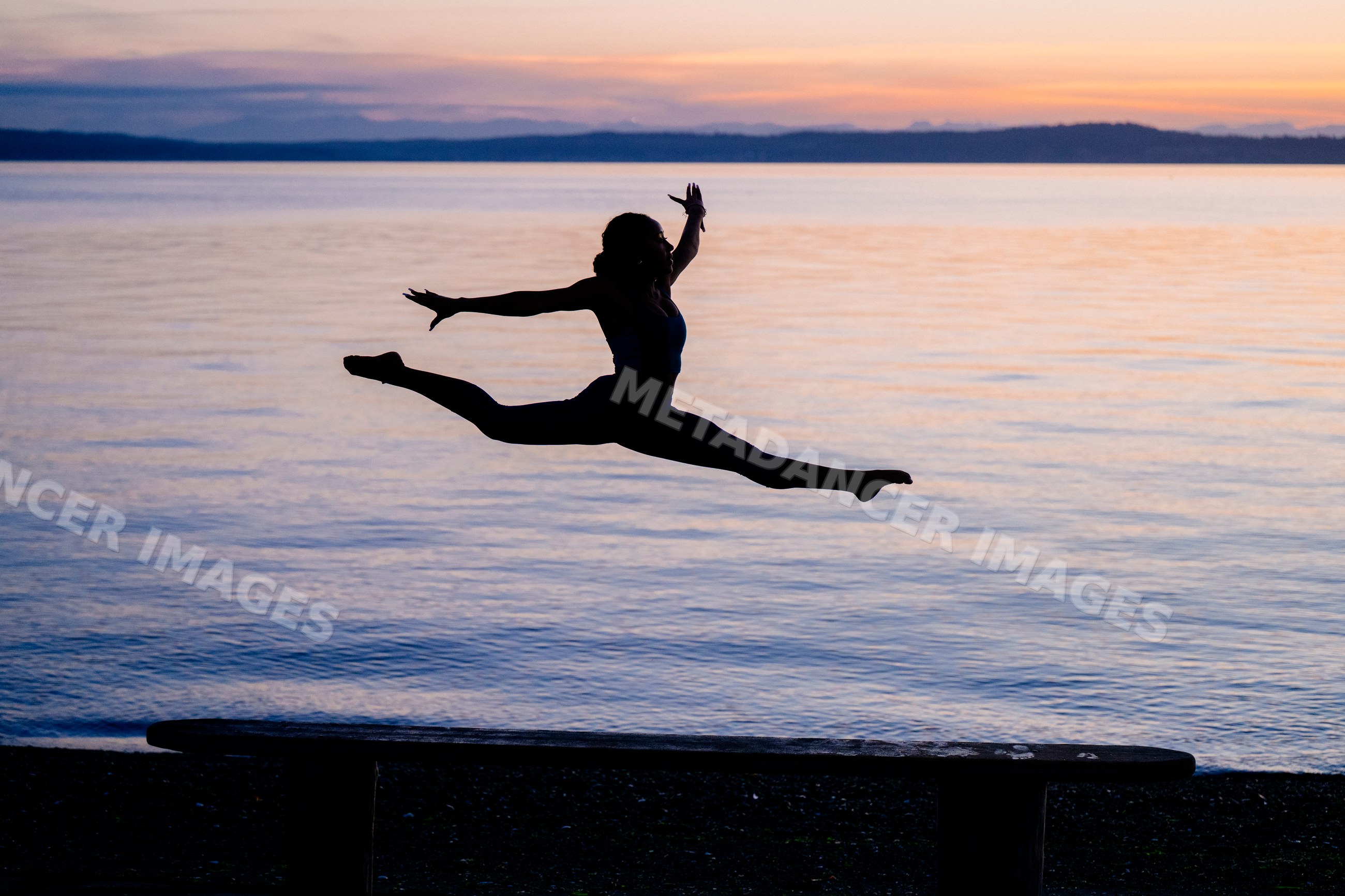 Hispanic woman performing acrobatic split jump outdoors by a lake