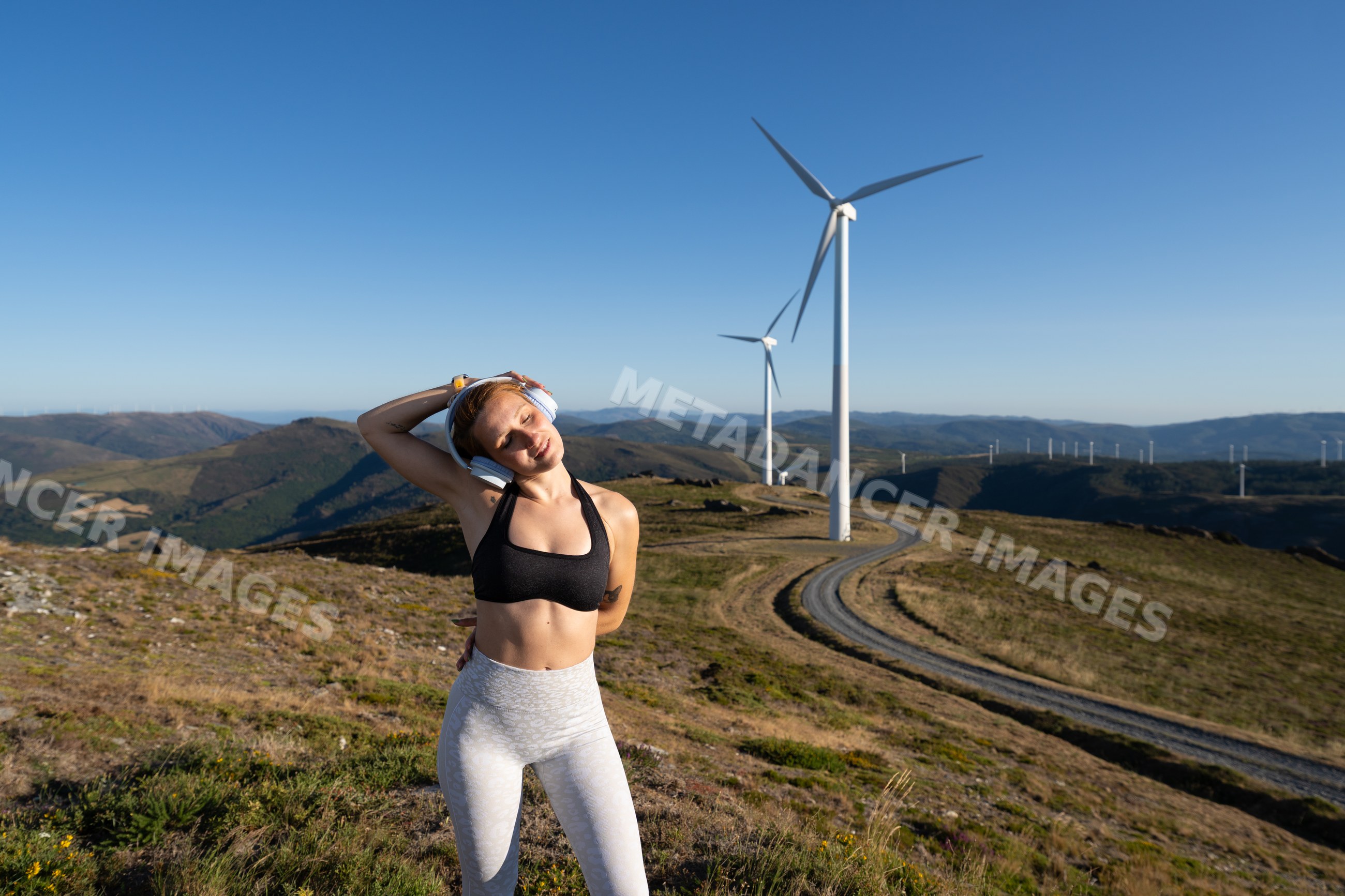 A white woman stretches her neck near wind turbines in Galicia, Spain