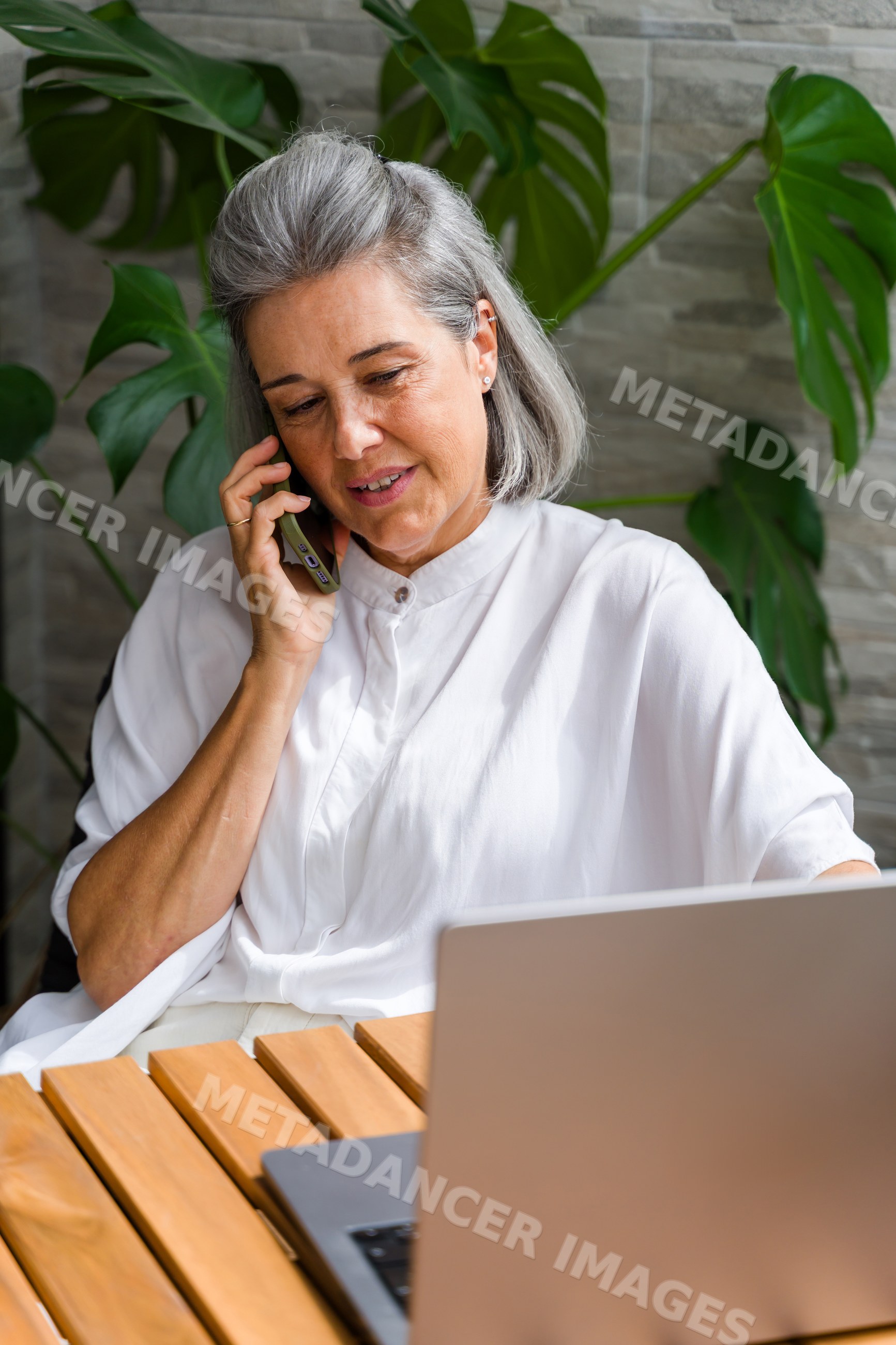 White Woman talking on phone using laptop indoors by plants