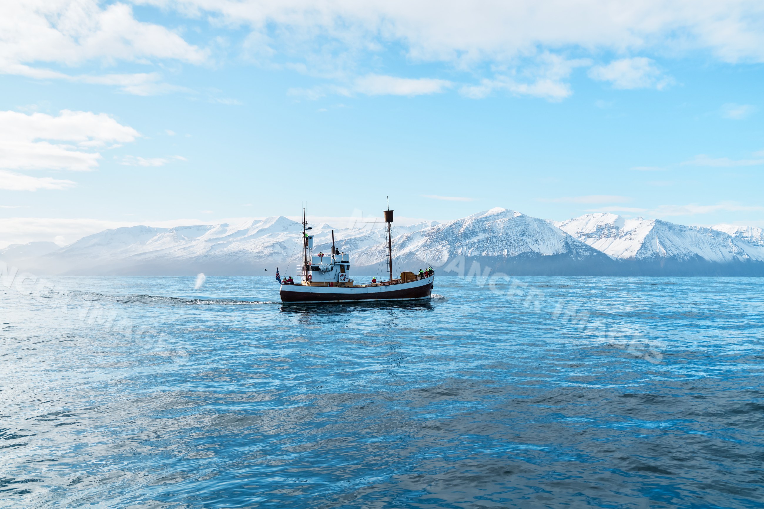 A fishing boat sails on calm ocean waters with snowy mountains