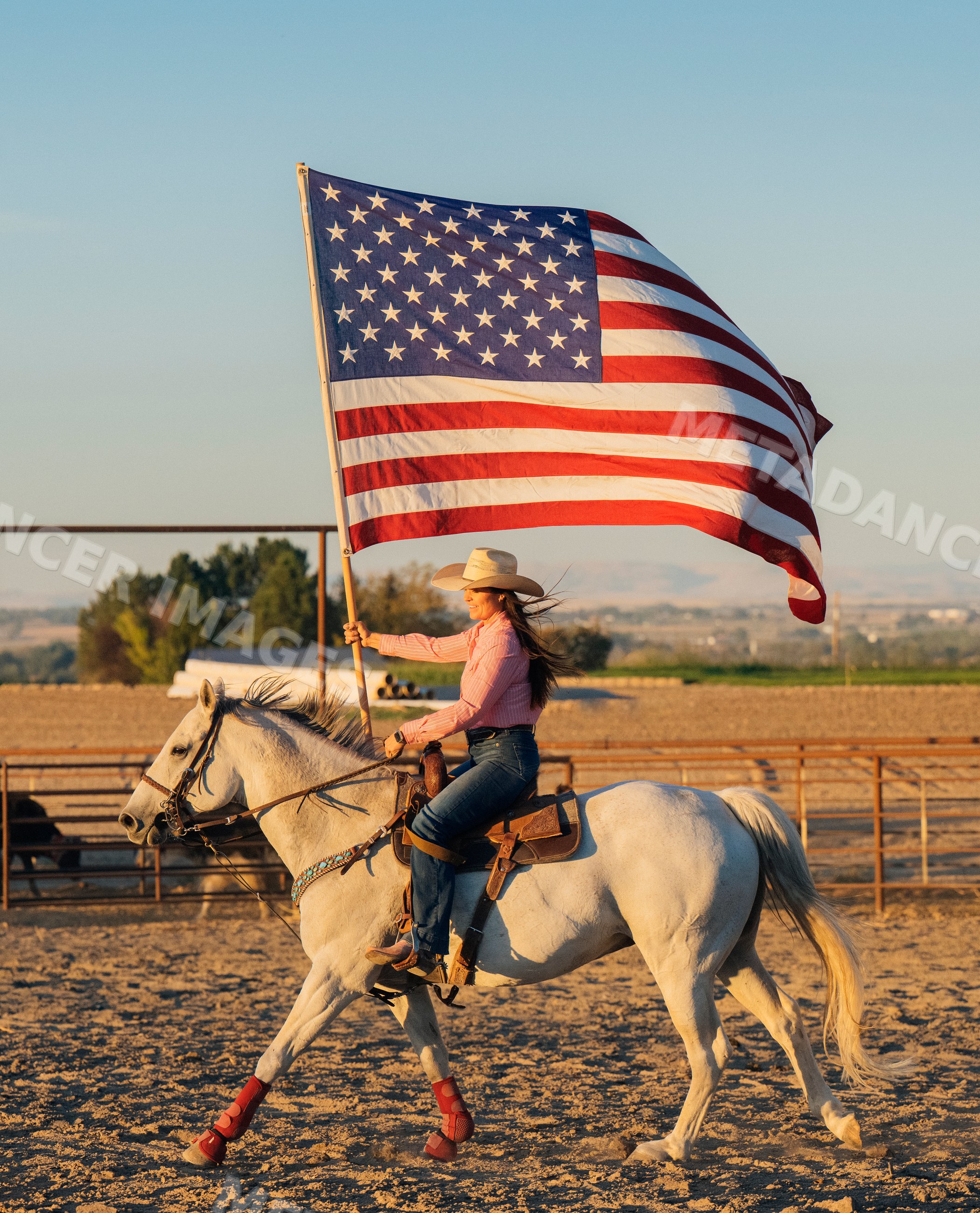 Woman riding white horse waving american flag in outdoor arena
