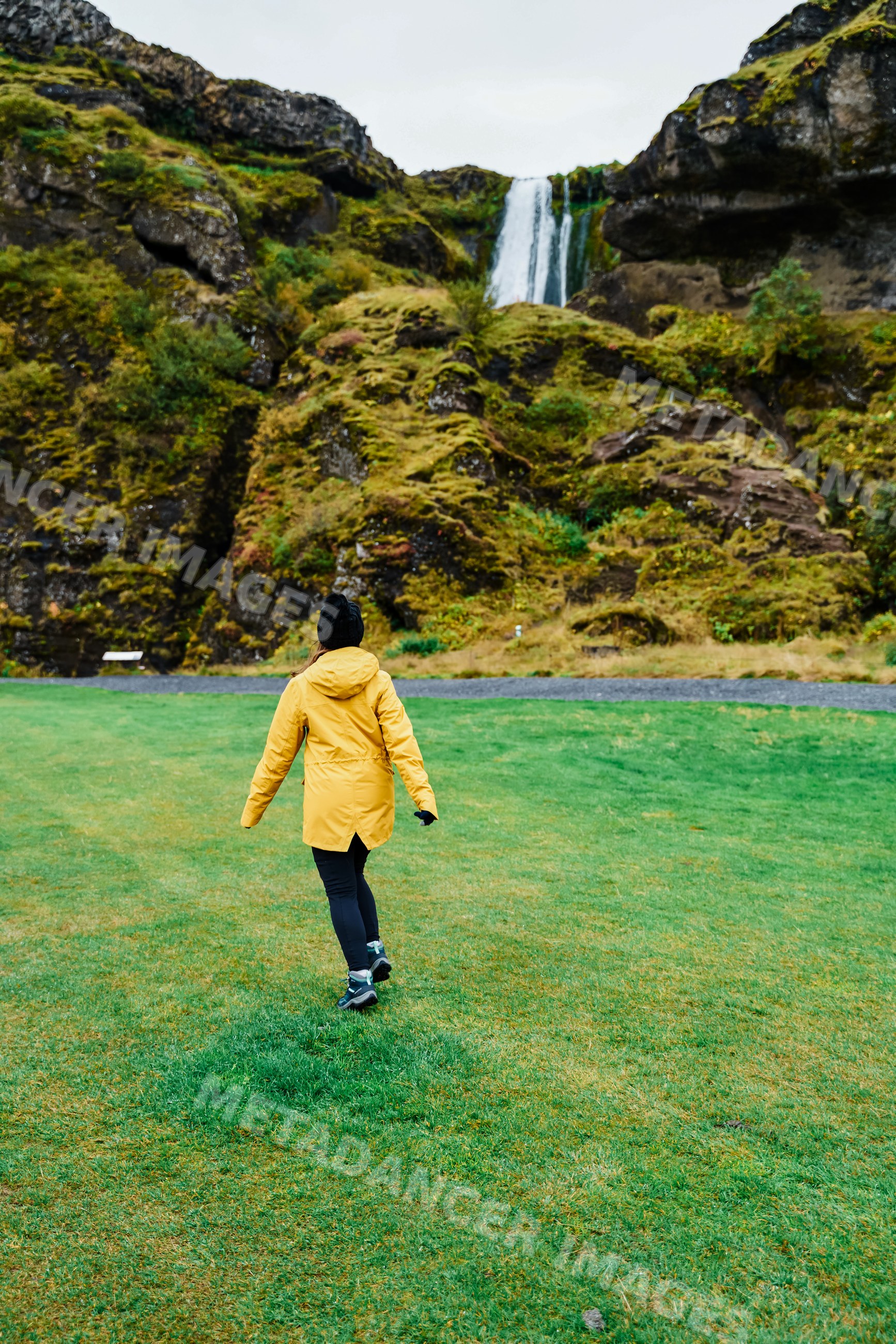 A white woman walks through grassy field toward a waterfall