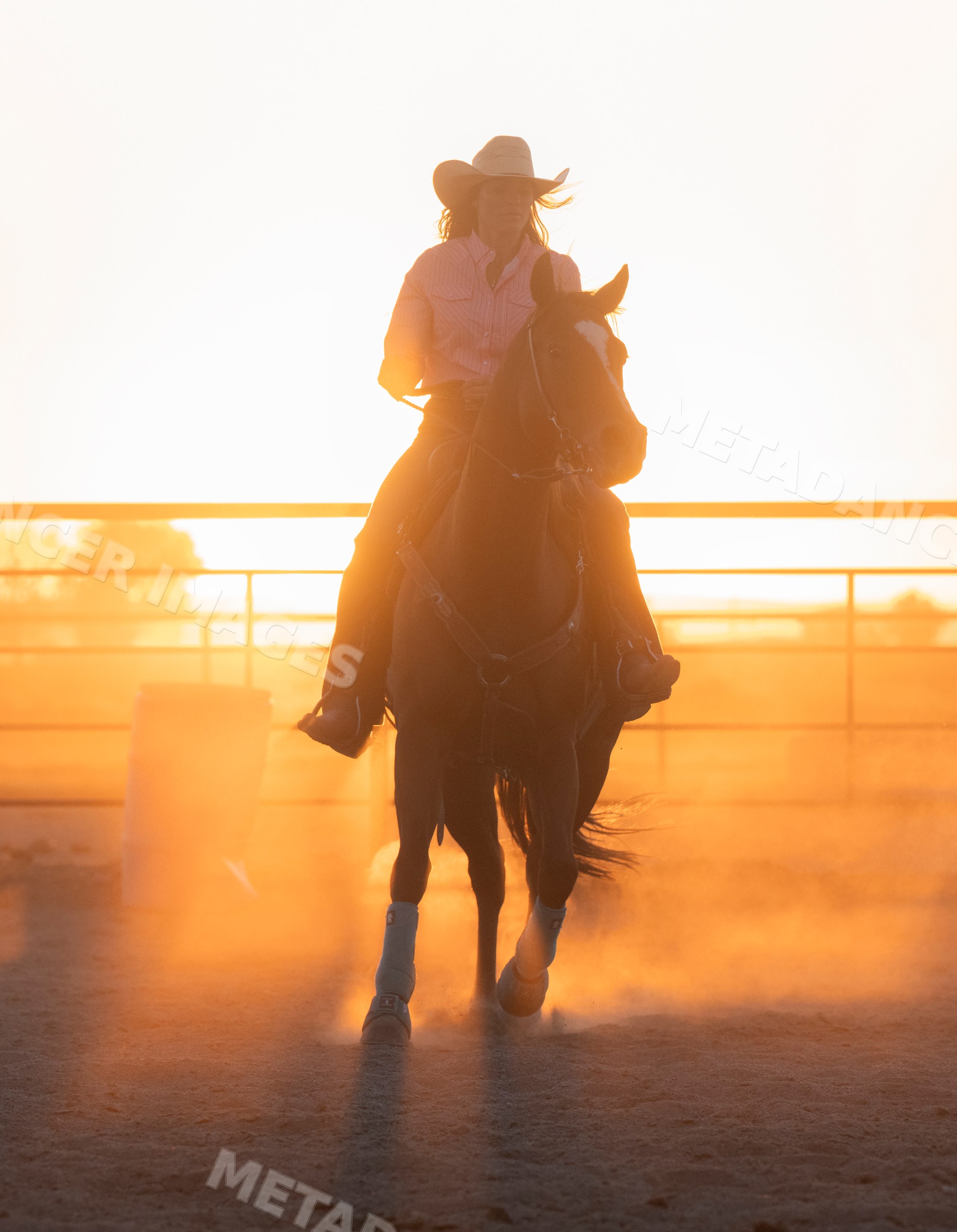 White woman riding horse at sunset in dusty outdoor riding arena