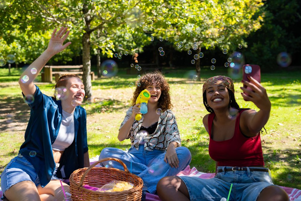 Friends playing with bubbles during a sunny picnic in a park in Spain