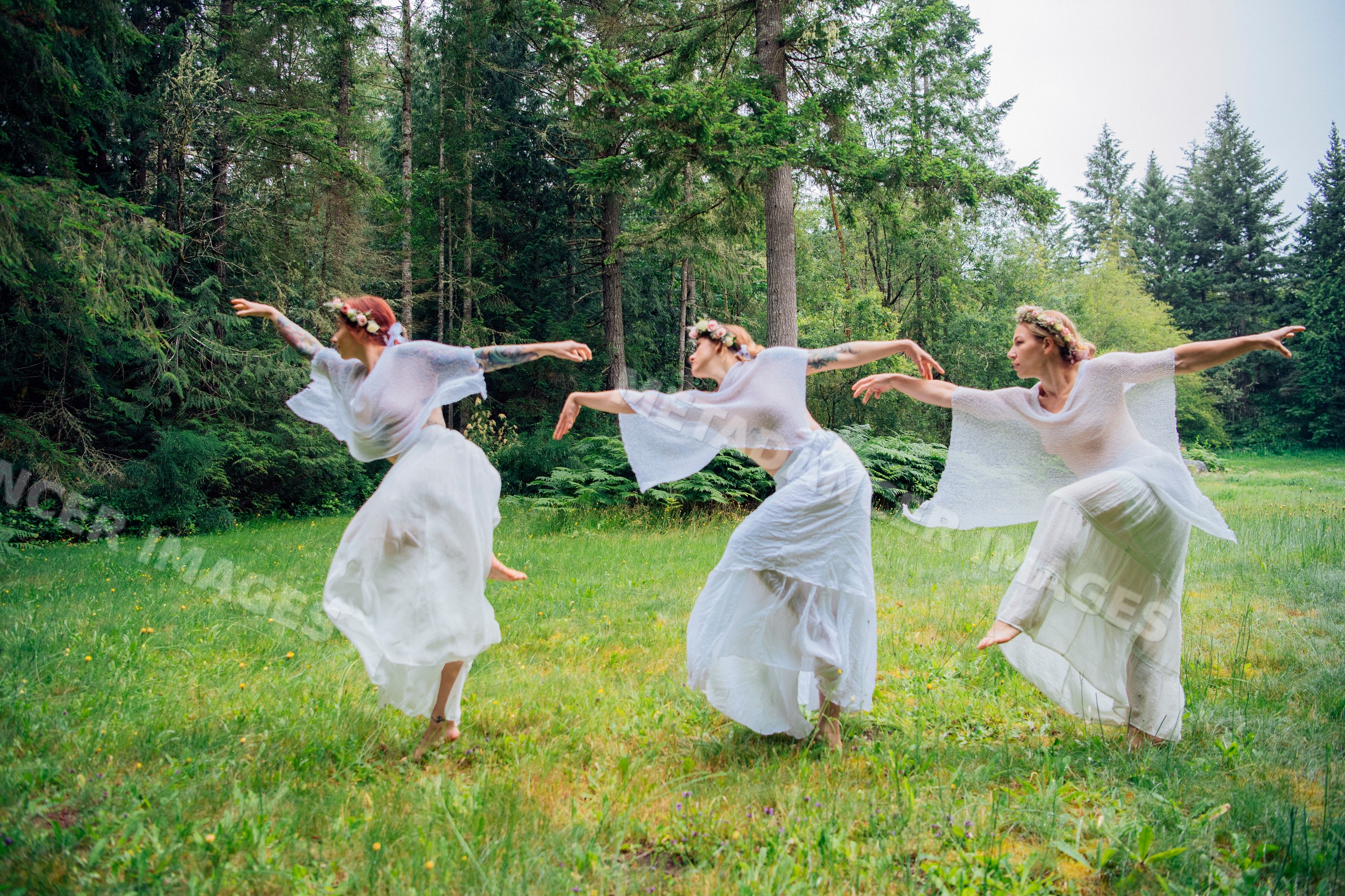 Women dancing barefoot in white dresses with flower crowns in a forest