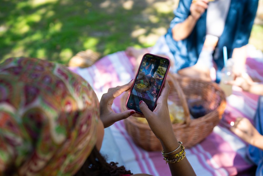 White and African American woman capturing picnic food basket photo
