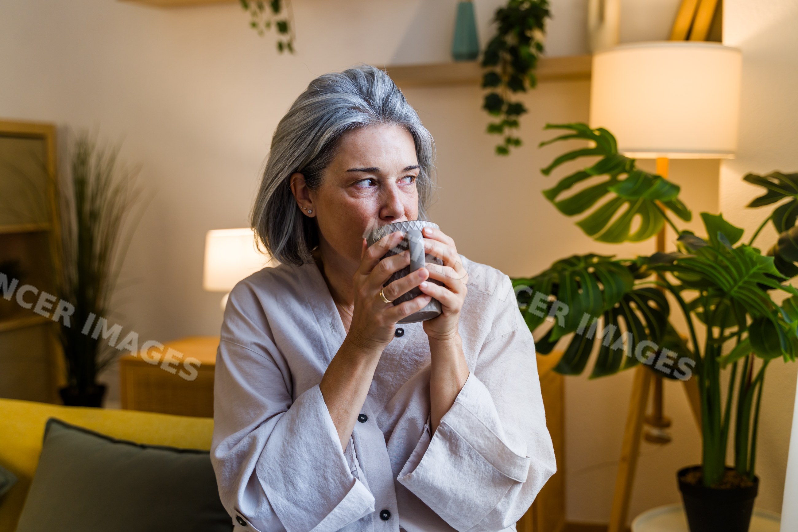 White woman drinking hot beverage in cozy living room interior