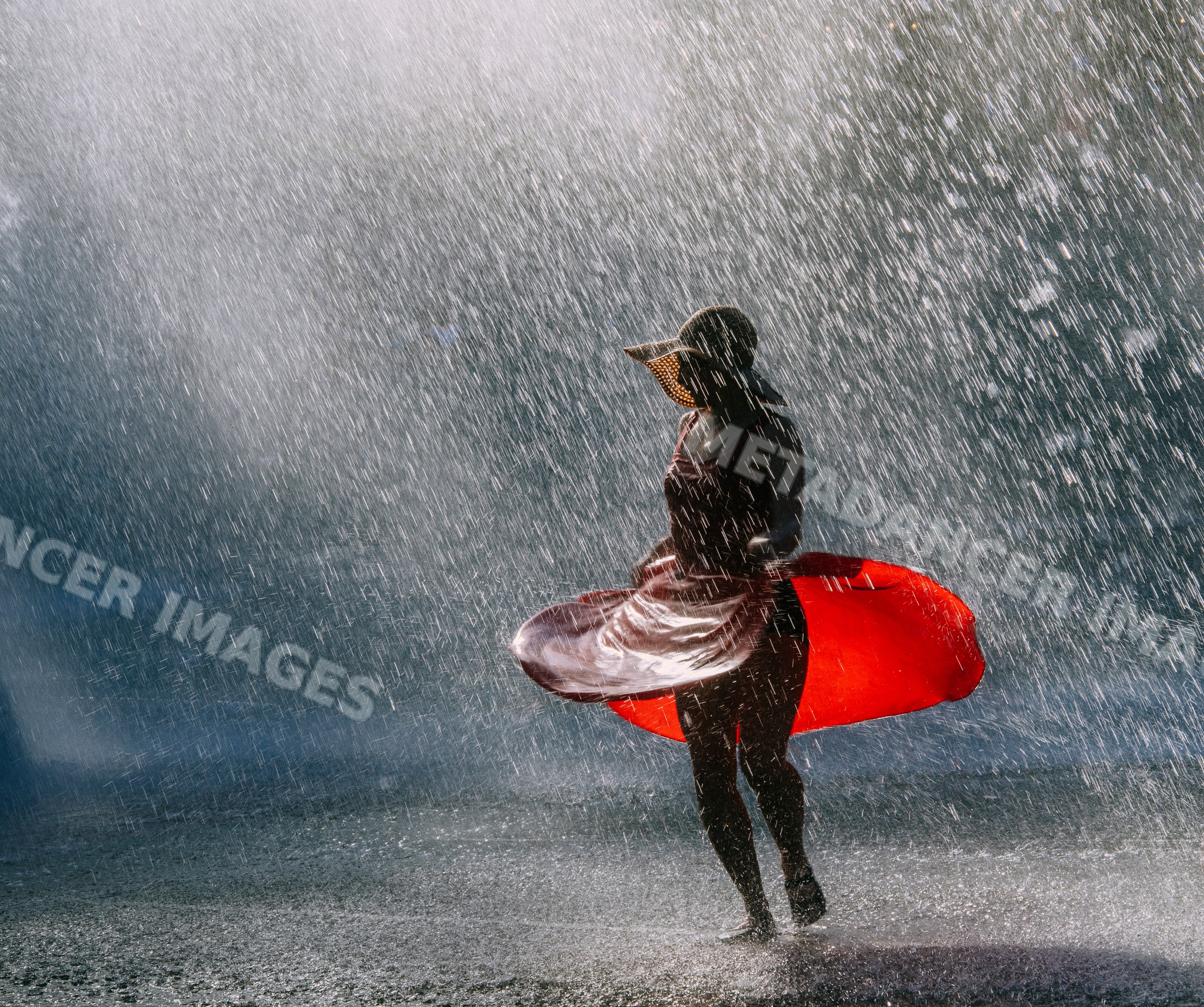 White woman dancing in water spray wearing red dress and sun hat