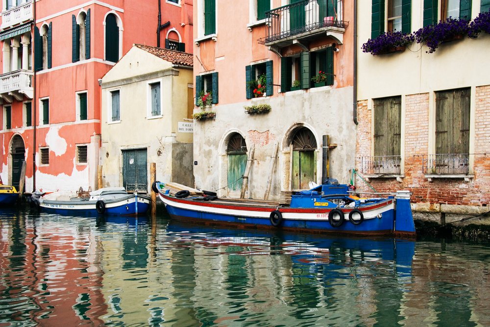 Boats moored on canal beside historic colorful buildings in venice