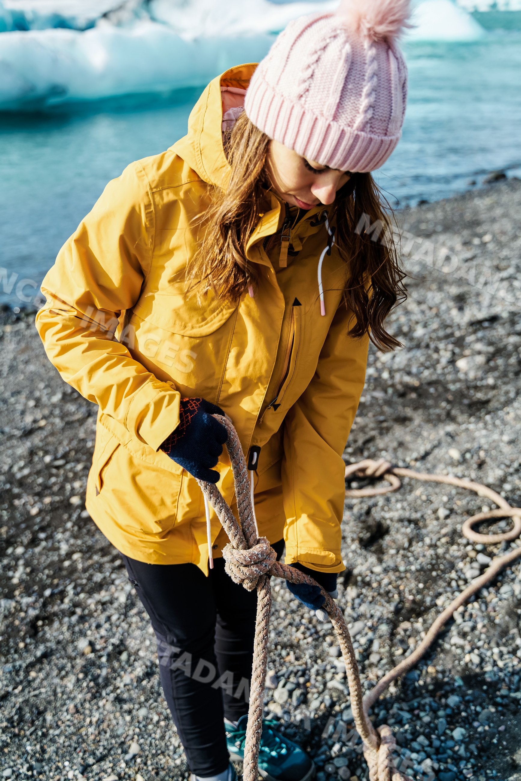 A white woman ties a rope knot on a gravel beach by the water