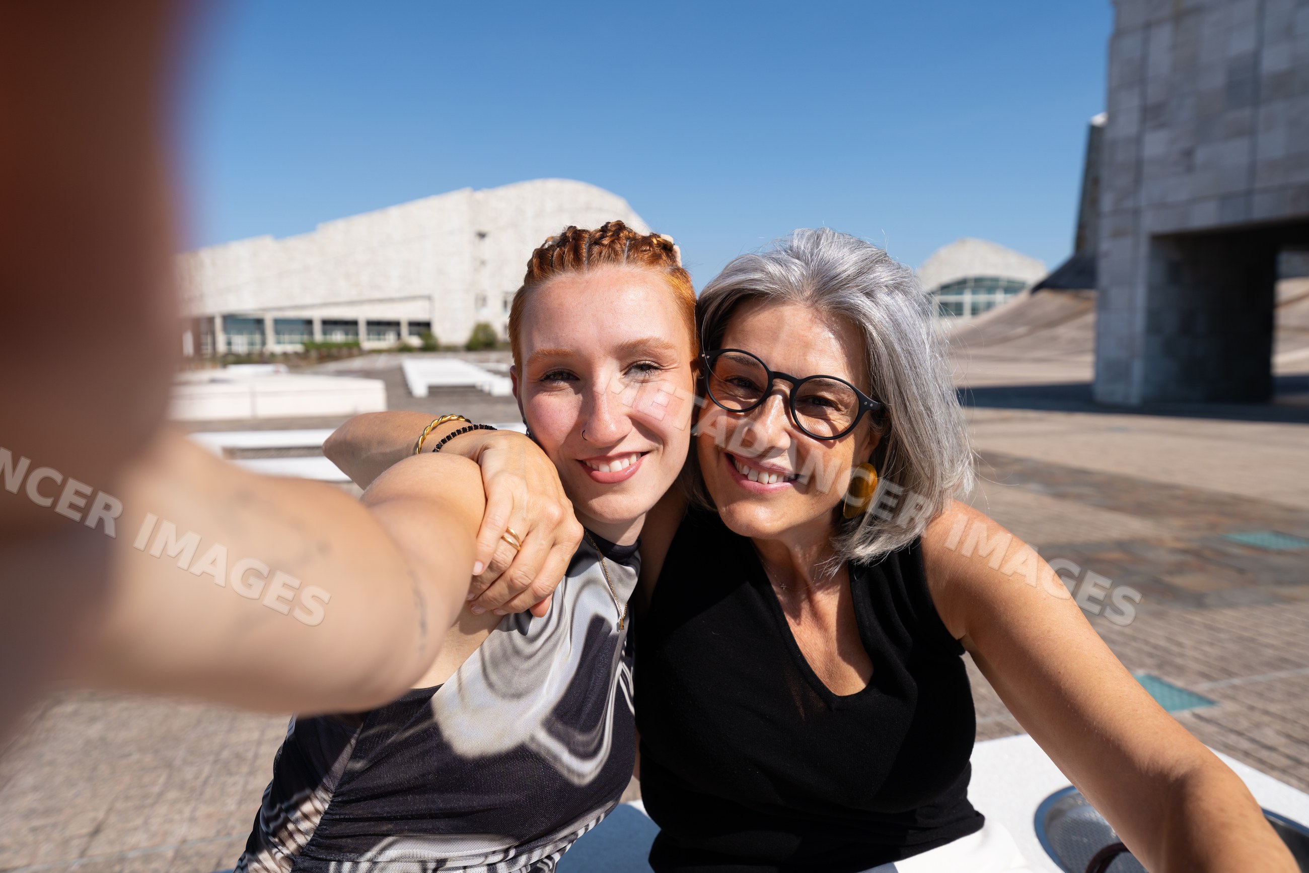 Two white women smiling and taking an outdoor selfie in urban Spain