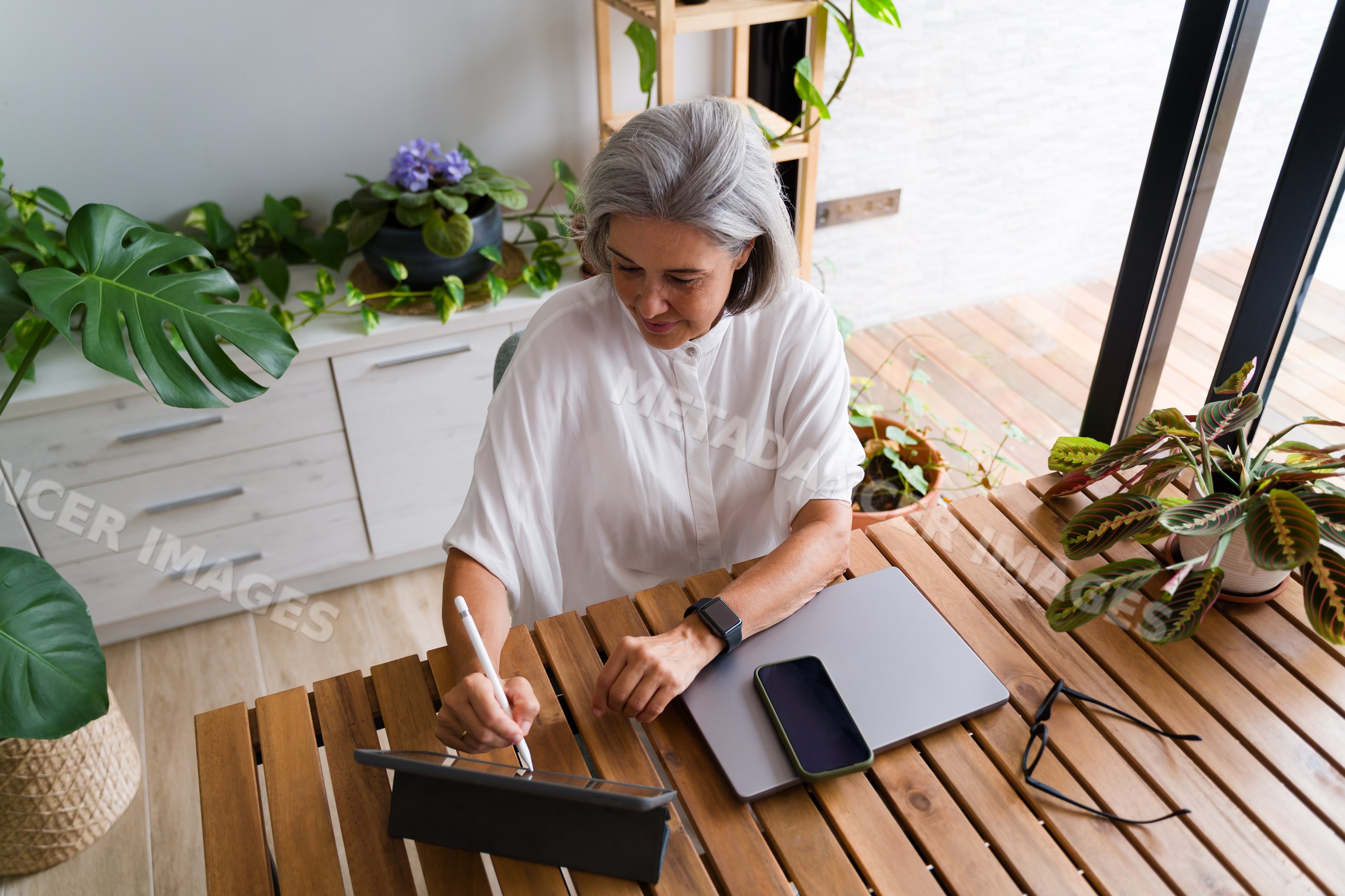 White Woman working on tablet in home office surrounded by plants