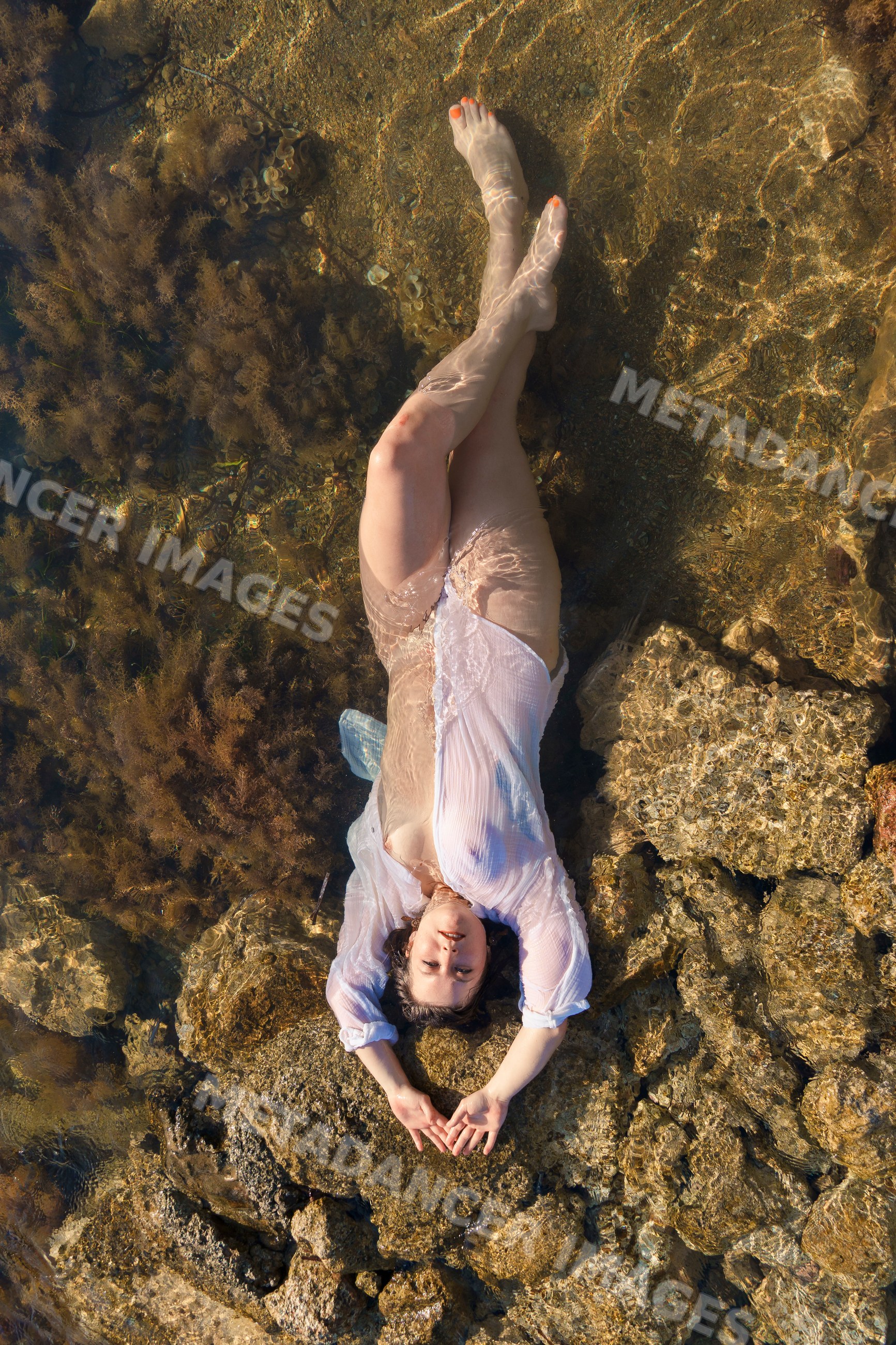 White woman relaxing in shallow water on rocks surrounded by seaweed