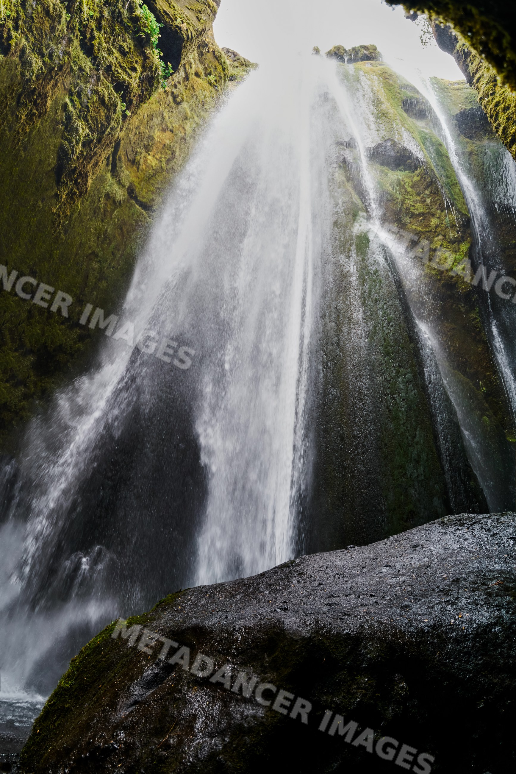 A moss-covered rocky waterfall flows in a natural Iceland landscape