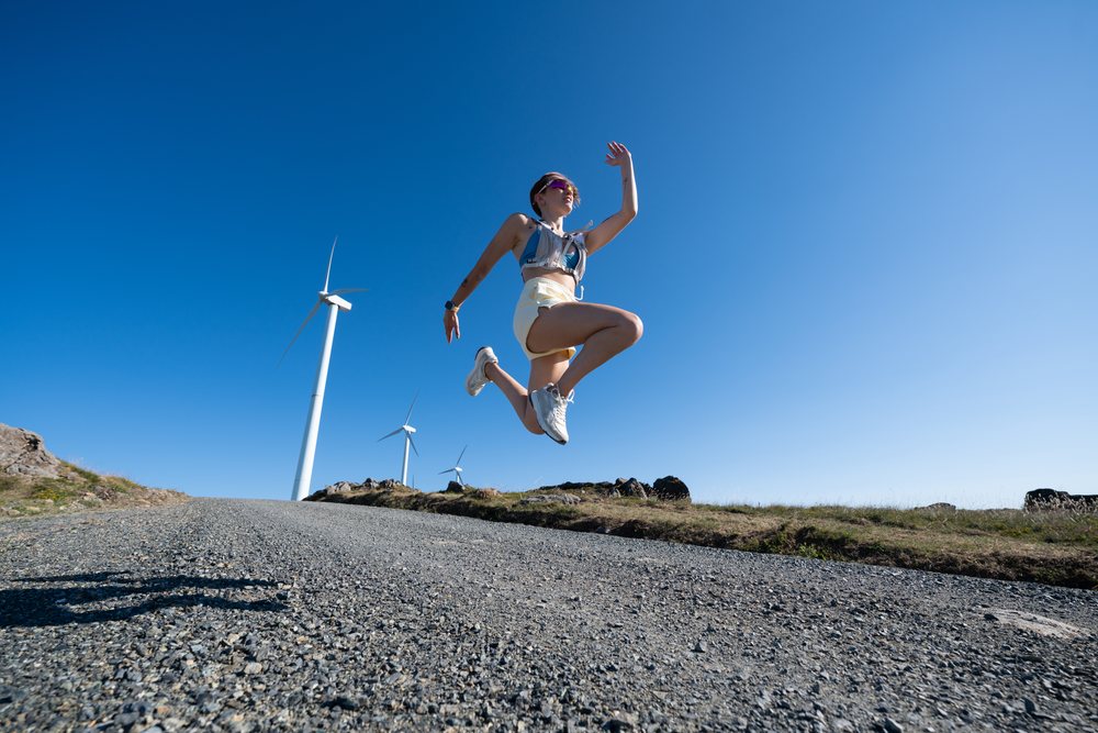 A white woman jumping outdoors near wind turbines in Galicia, Spain