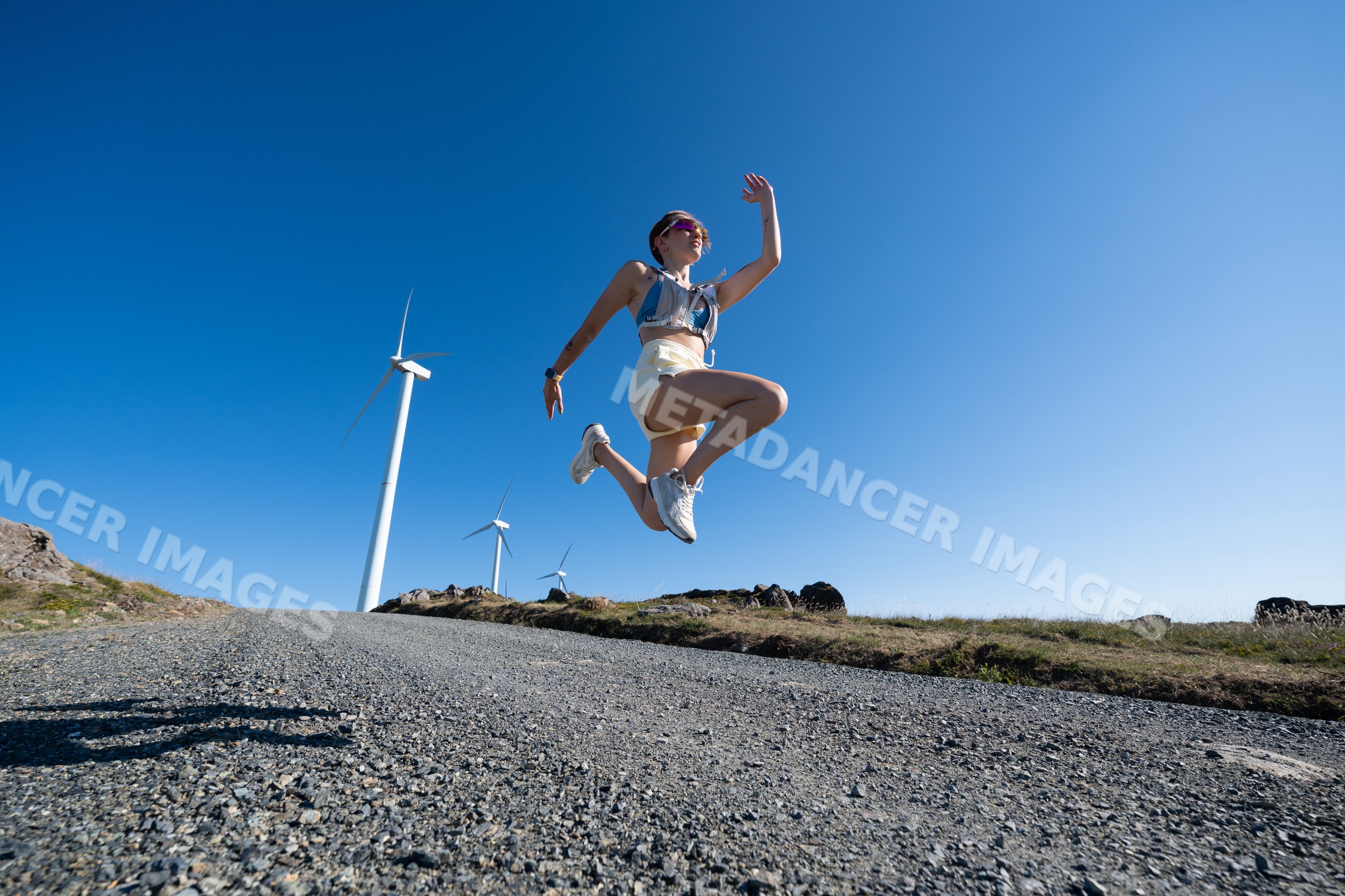 A white woman jumping outdoors near wind turbines in Galicia, Spain