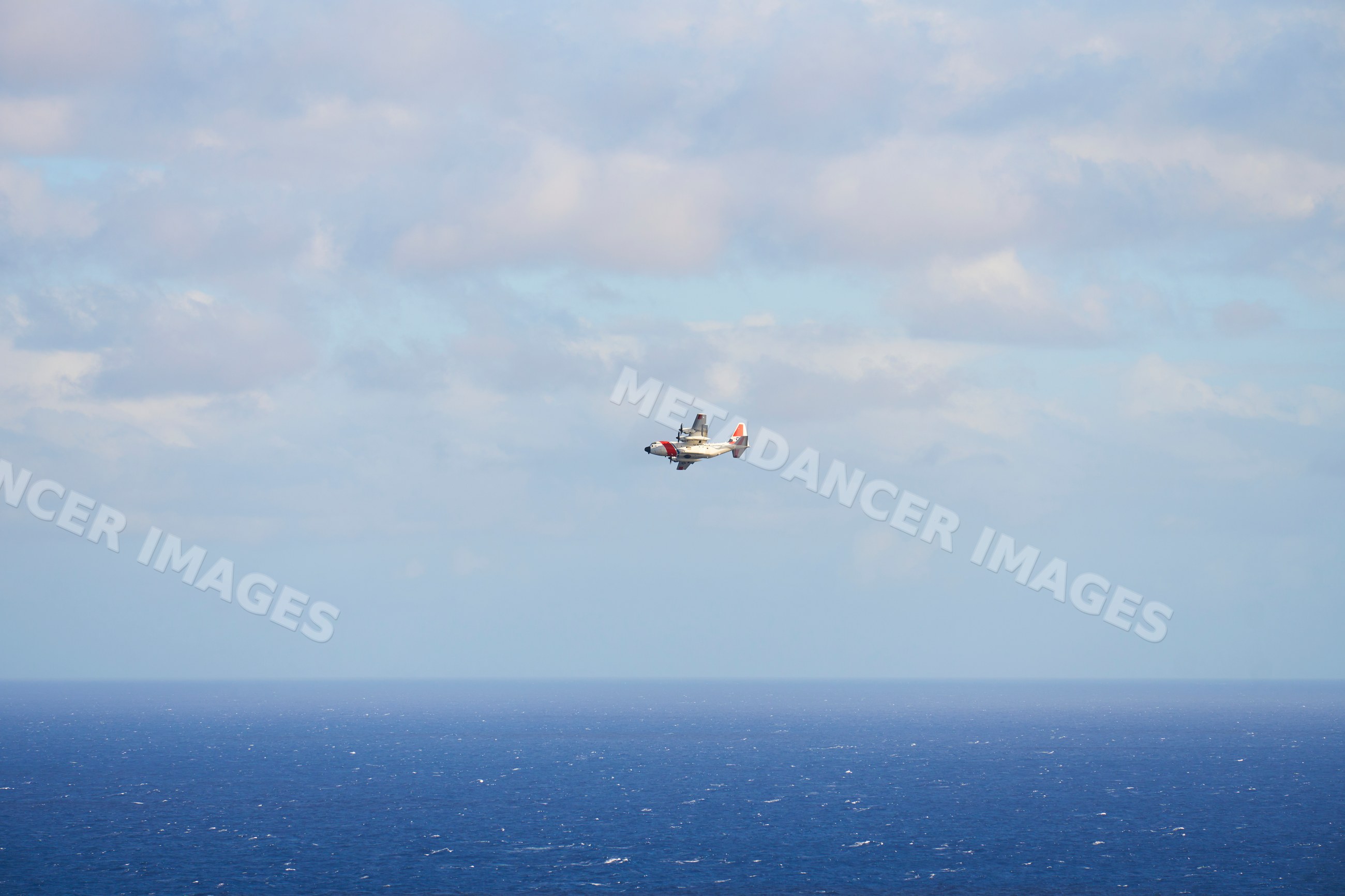 Airplane flying over ocean with distant horizon and clouds