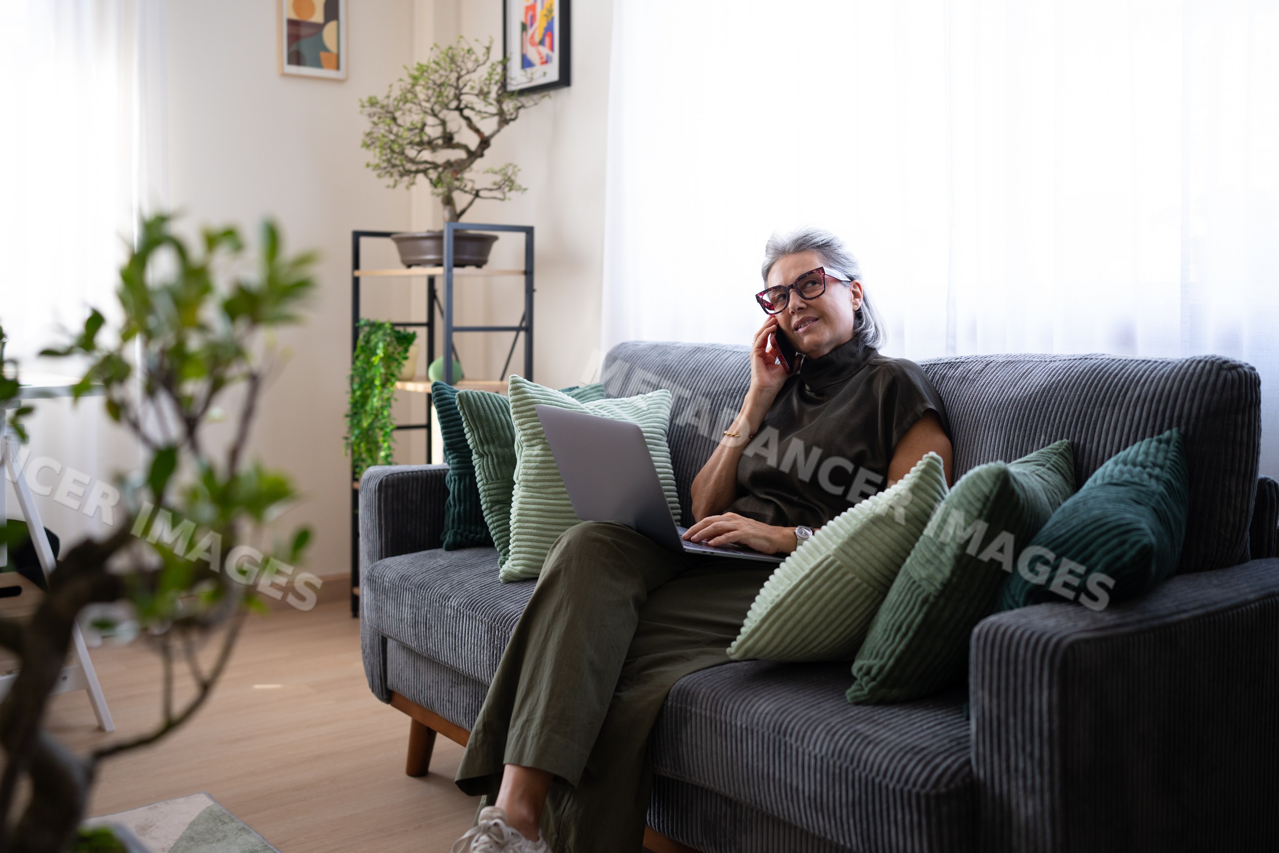 White woman talking on phone with laptop on couch