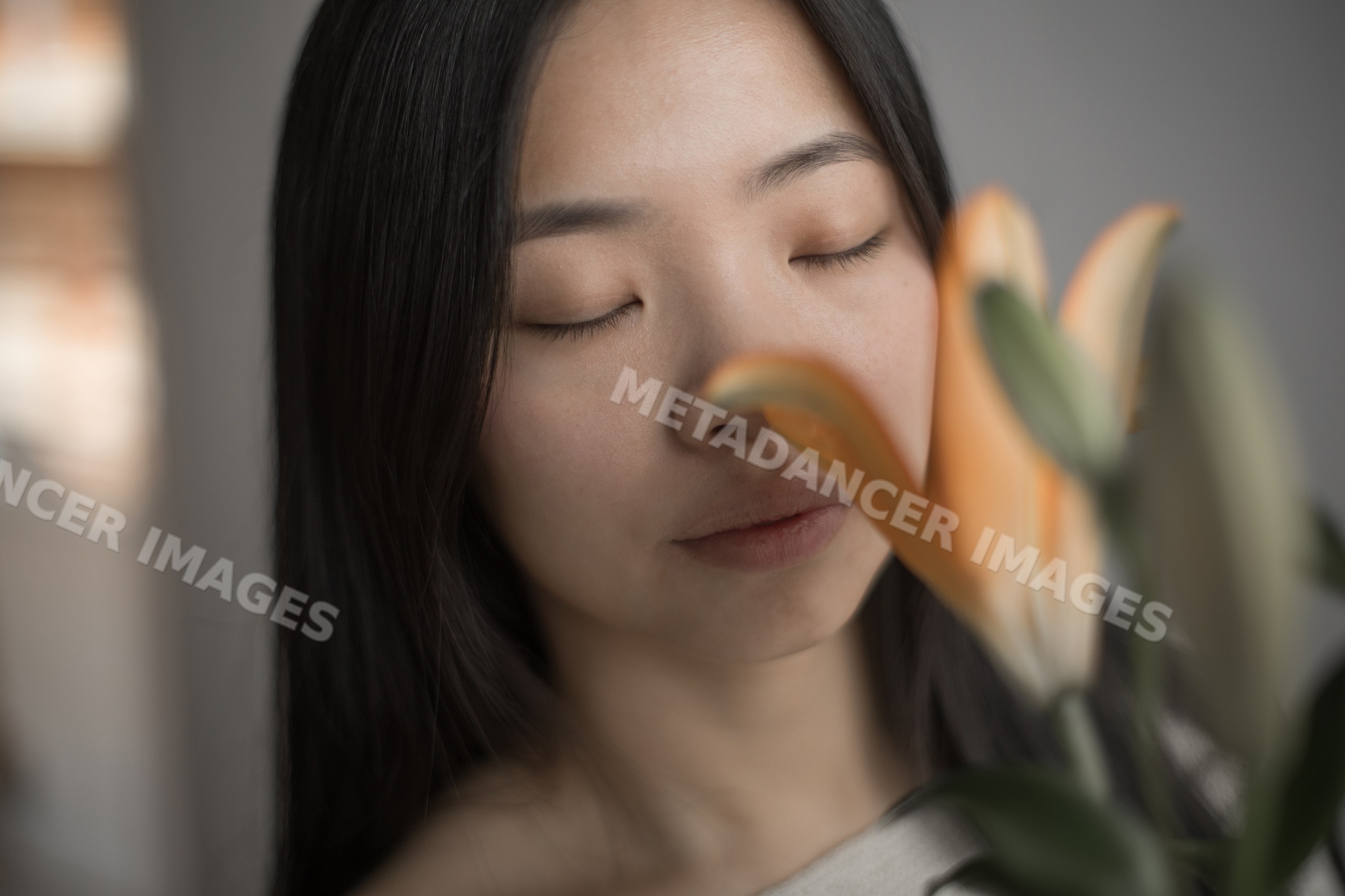 Southeast Asian woman with closed eyes holding a lily flower