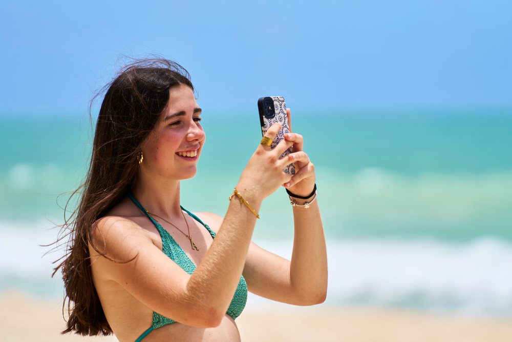 White woman taking a photo with smartphone on a sunny beach in Hawaii