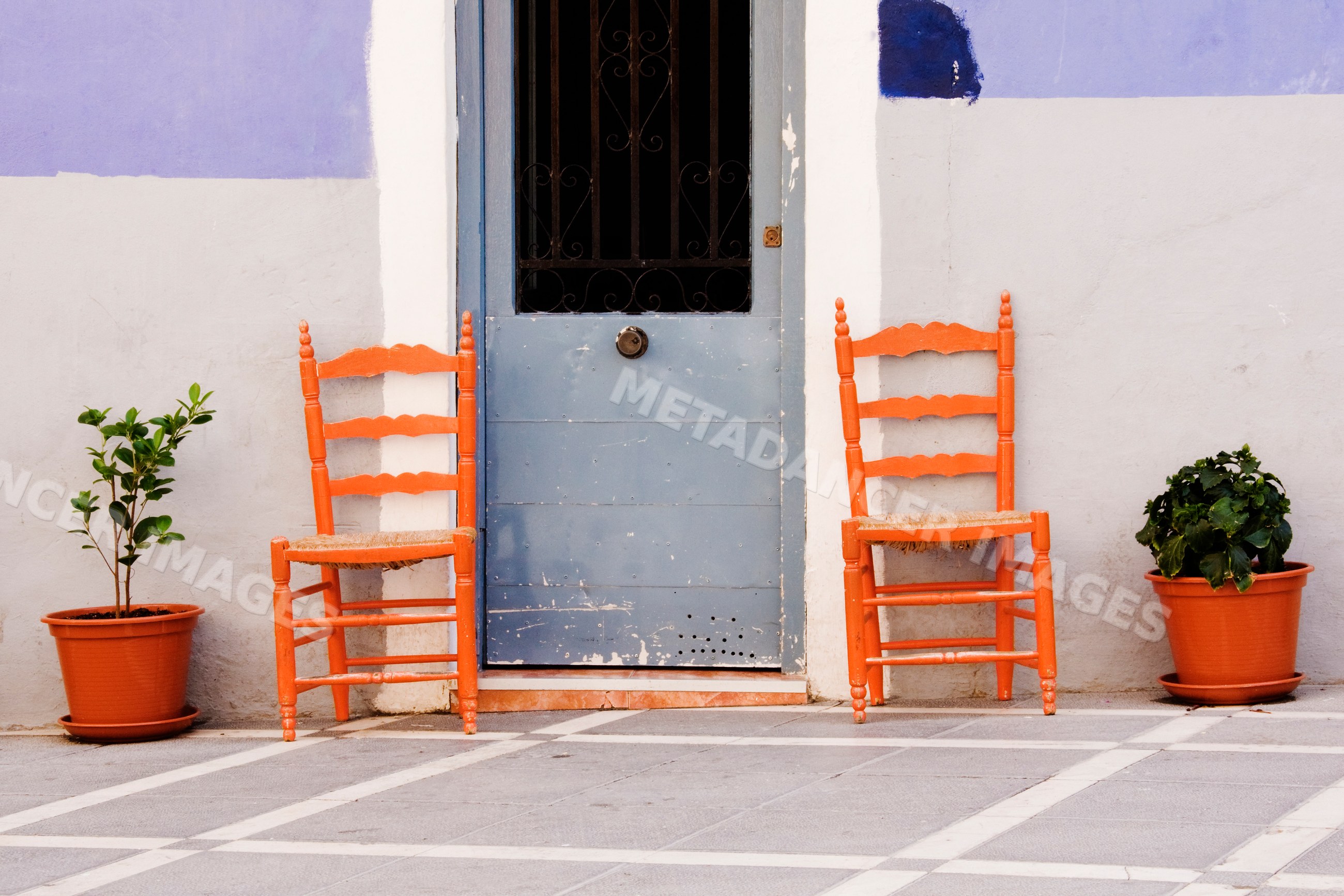 Two orange chairs beside blue door on painted exterior wall, Spain