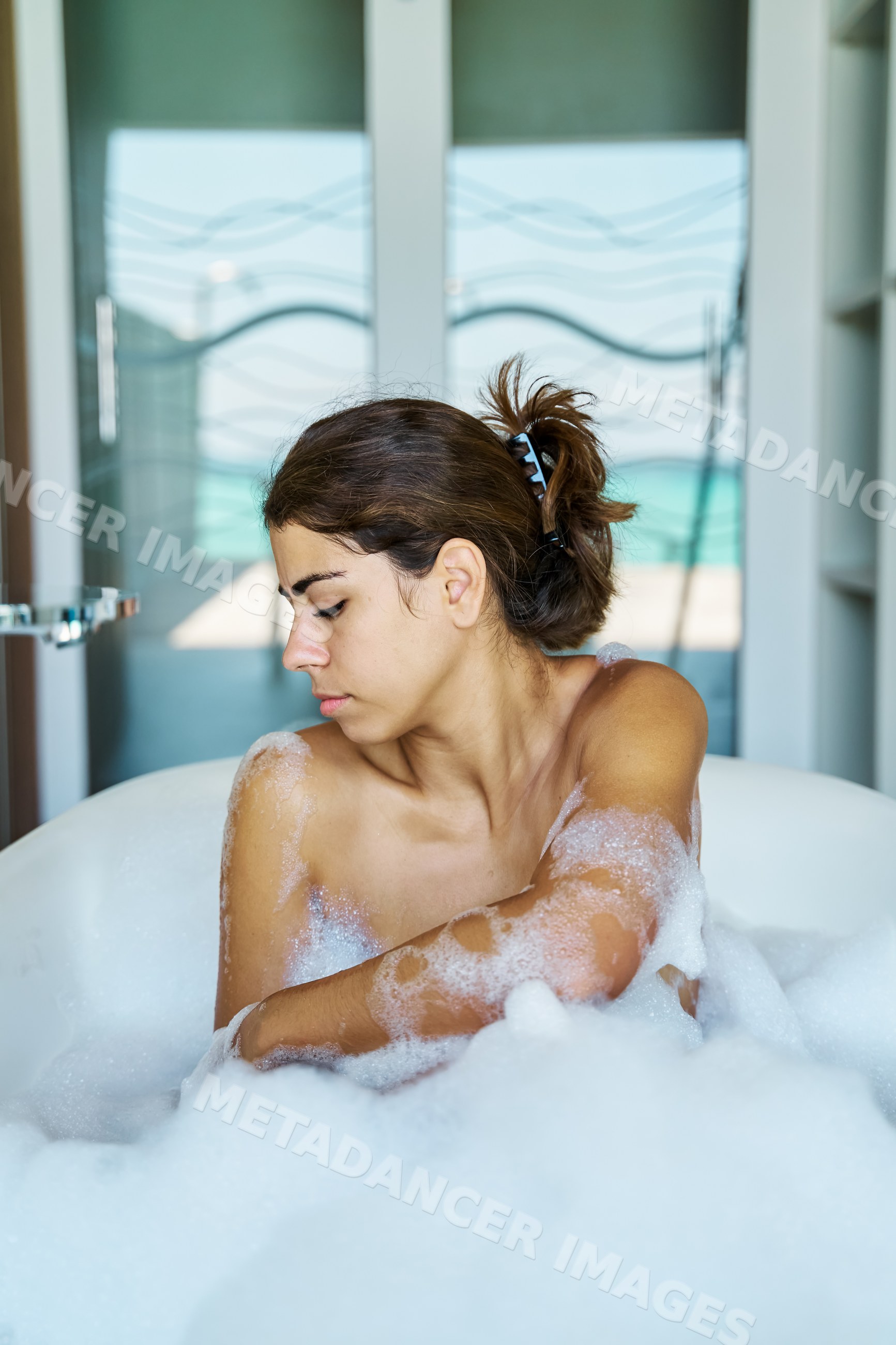 A young white woman relaxes in a bubble bath in a bathroom