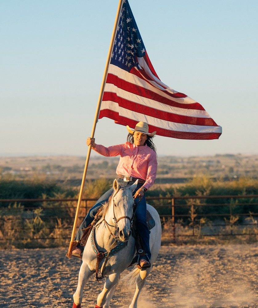 Woman riding white horse holding american flag in Southwest USA arena