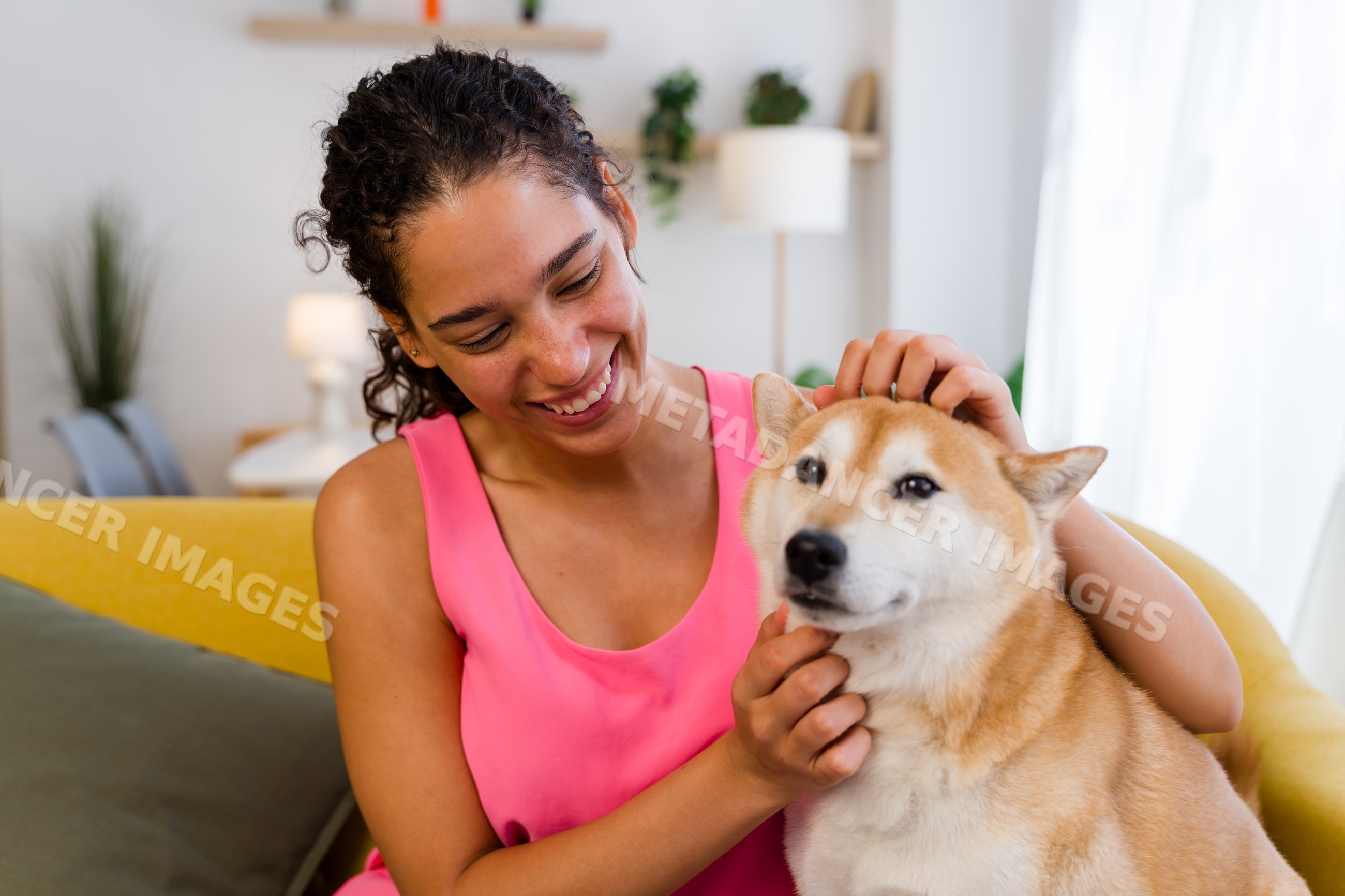 A Hispanic woman smiles while petting a dog indoors
