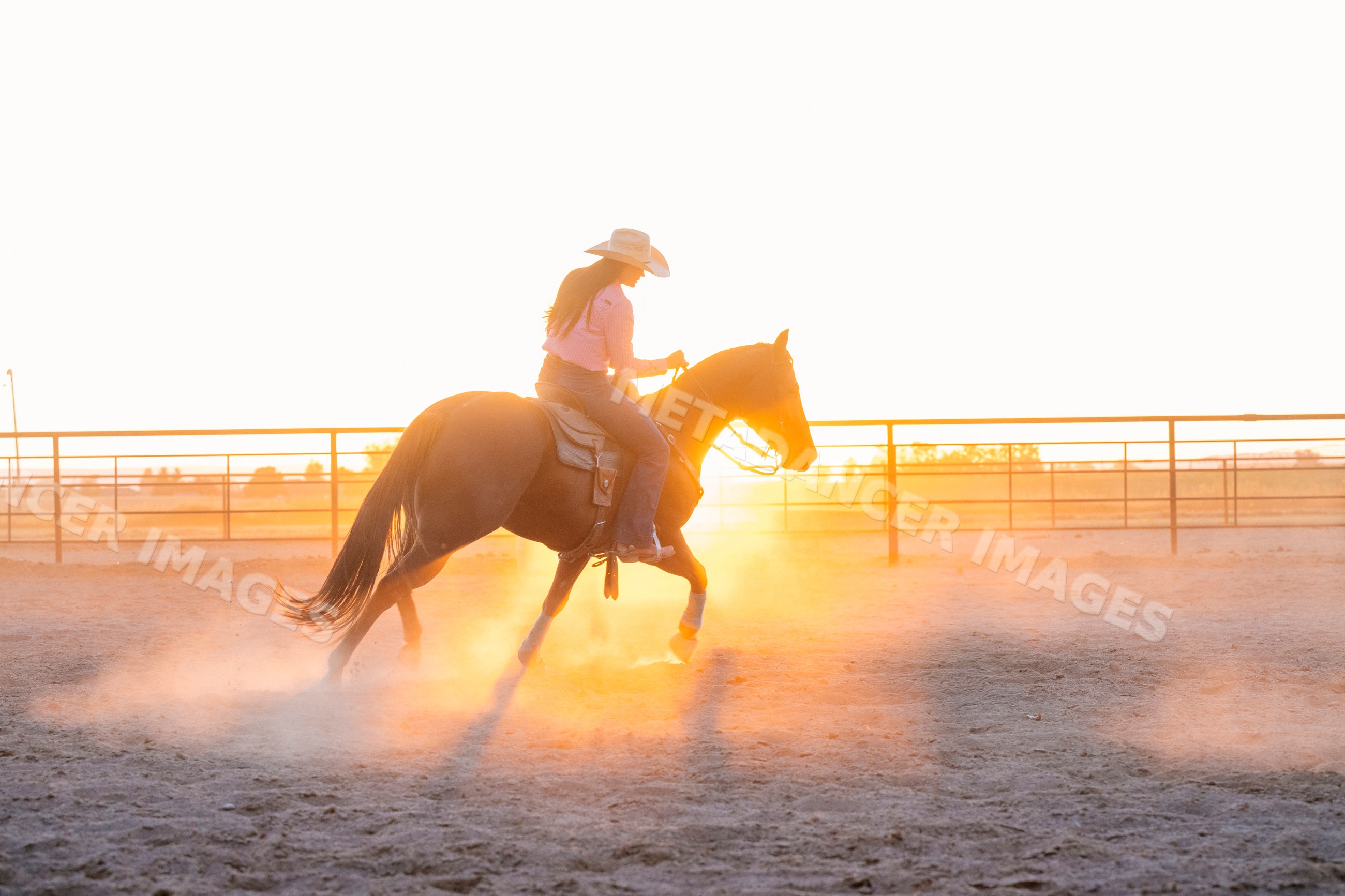 White woman riding horse in fenced arena at sunset in Southwest USA