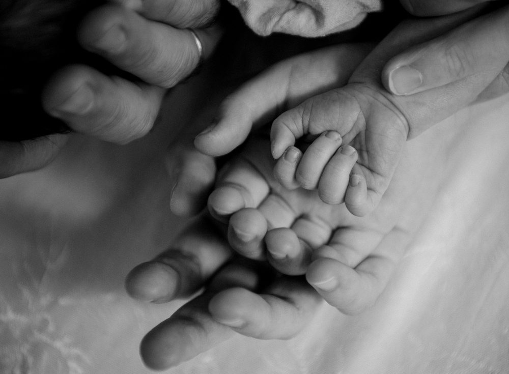 Newborn baby hand held by white adult hand in tender black