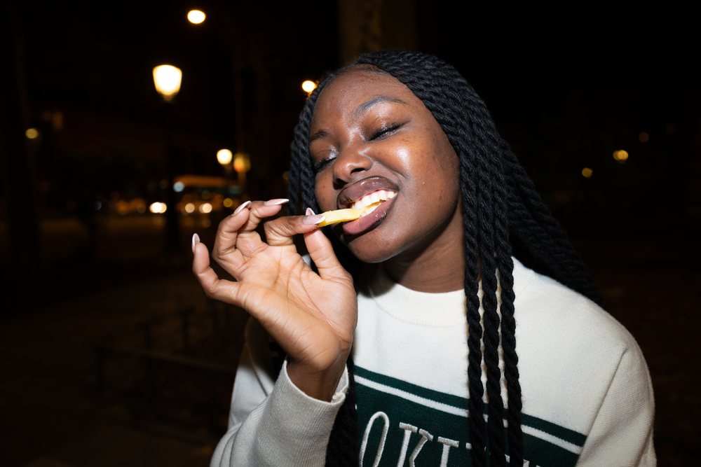 Black woman enjoying a french fry outside at night in Madrid, Spain