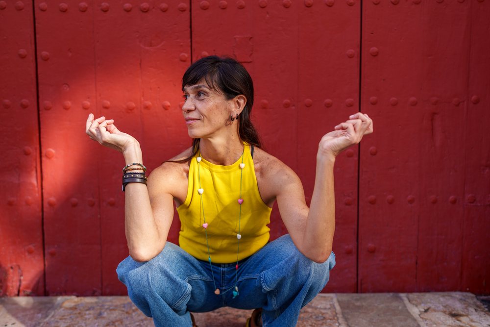 Hispanic woman squatting in yellow top and blue jeans by red door