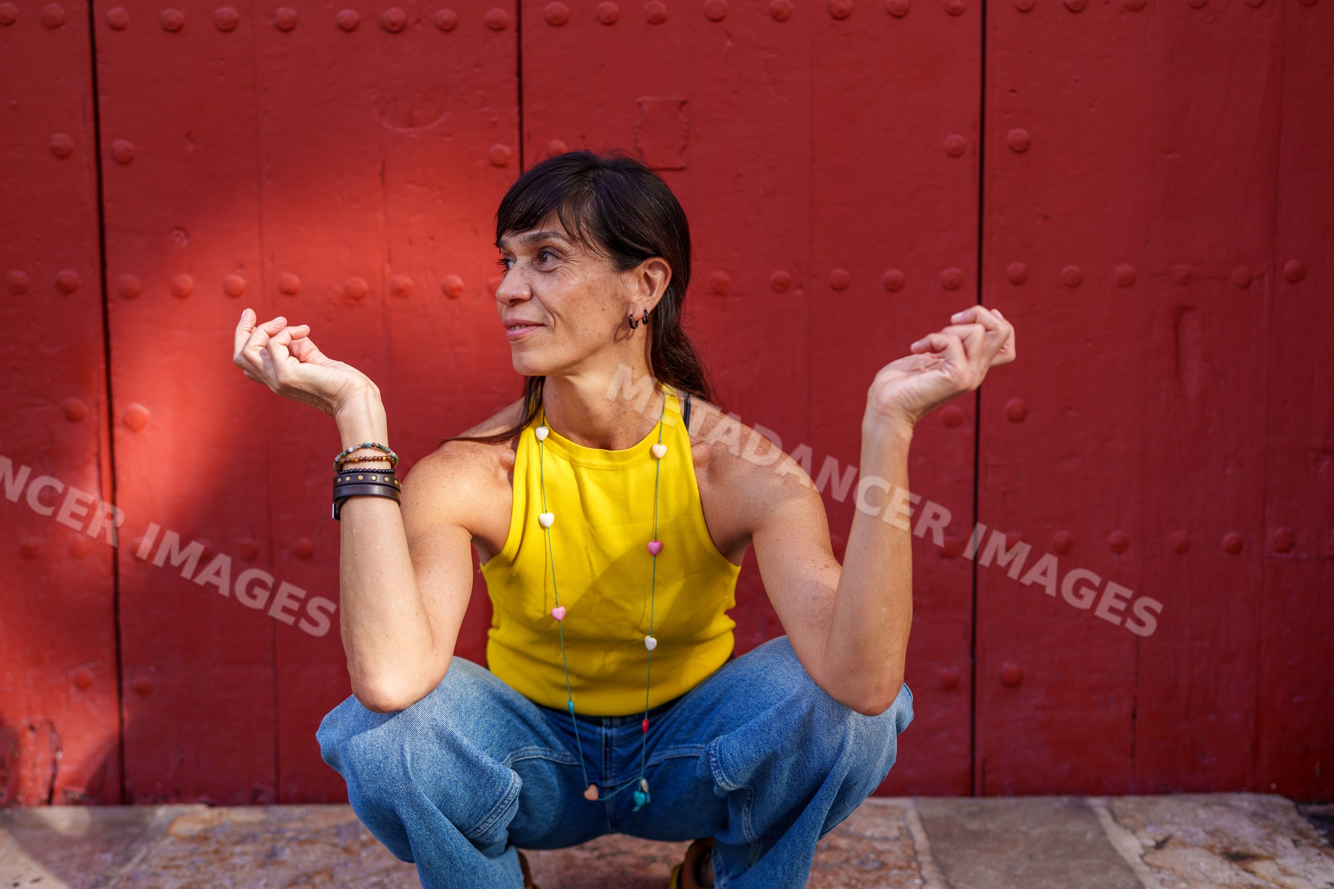 Hispanic woman squatting in yellow top and blue jeans by red door